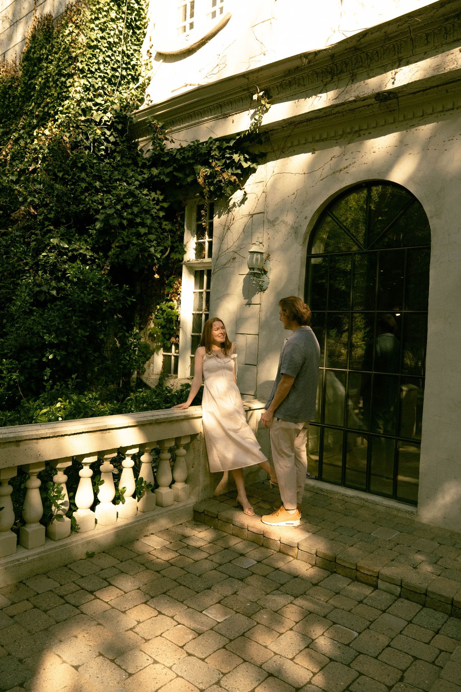 A couple sharing a joyful moment on a balcony with classic architectural details and climbing vines.