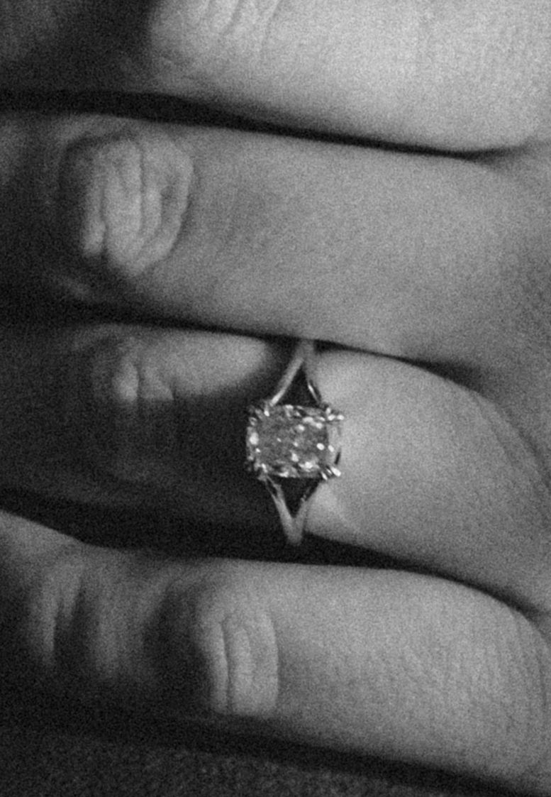 Close-up black and white photo of a hand wearing a solitaire diamond engagement ring on the ring finger.