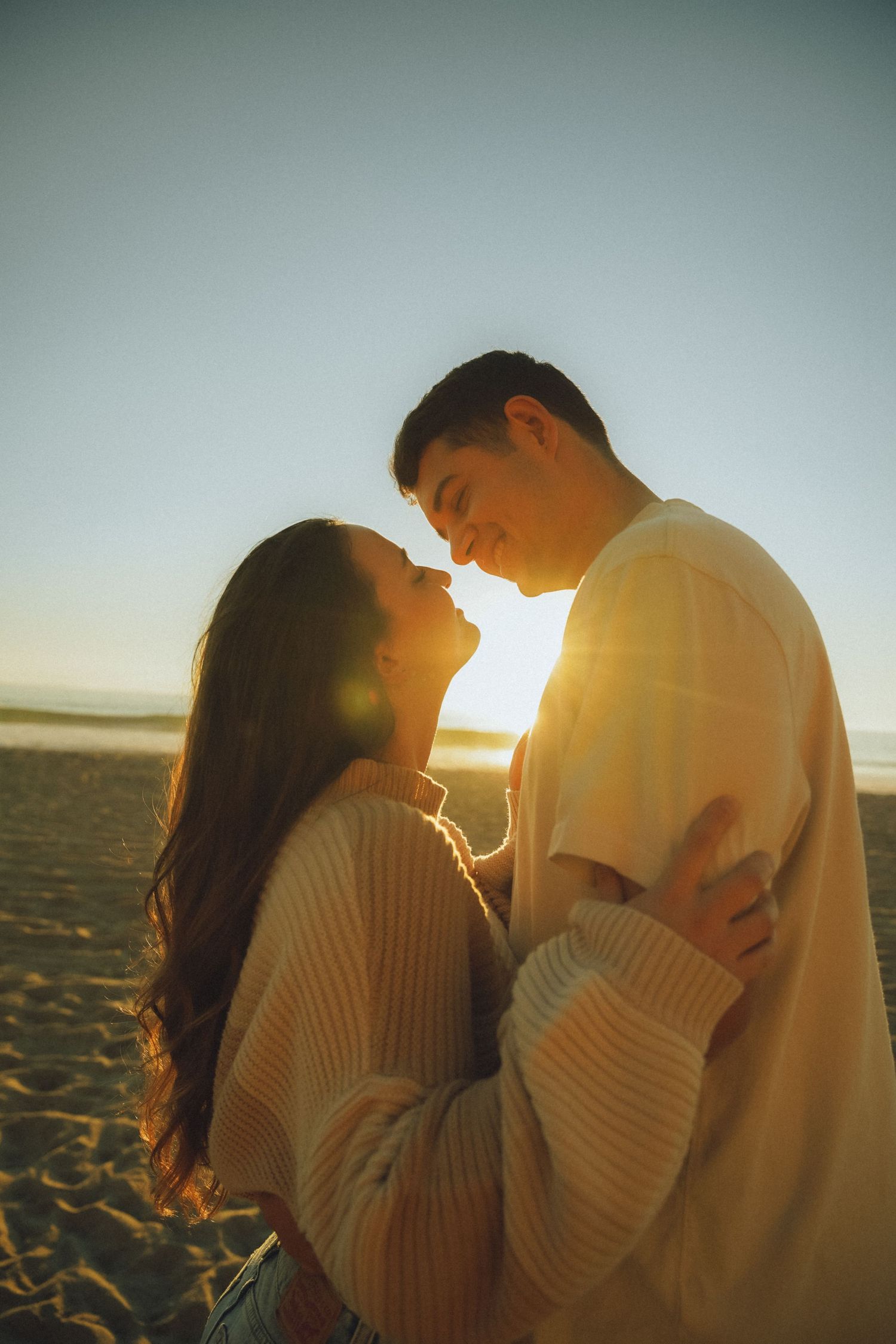 A couple shares an intimate moment on the beach during golden hour.