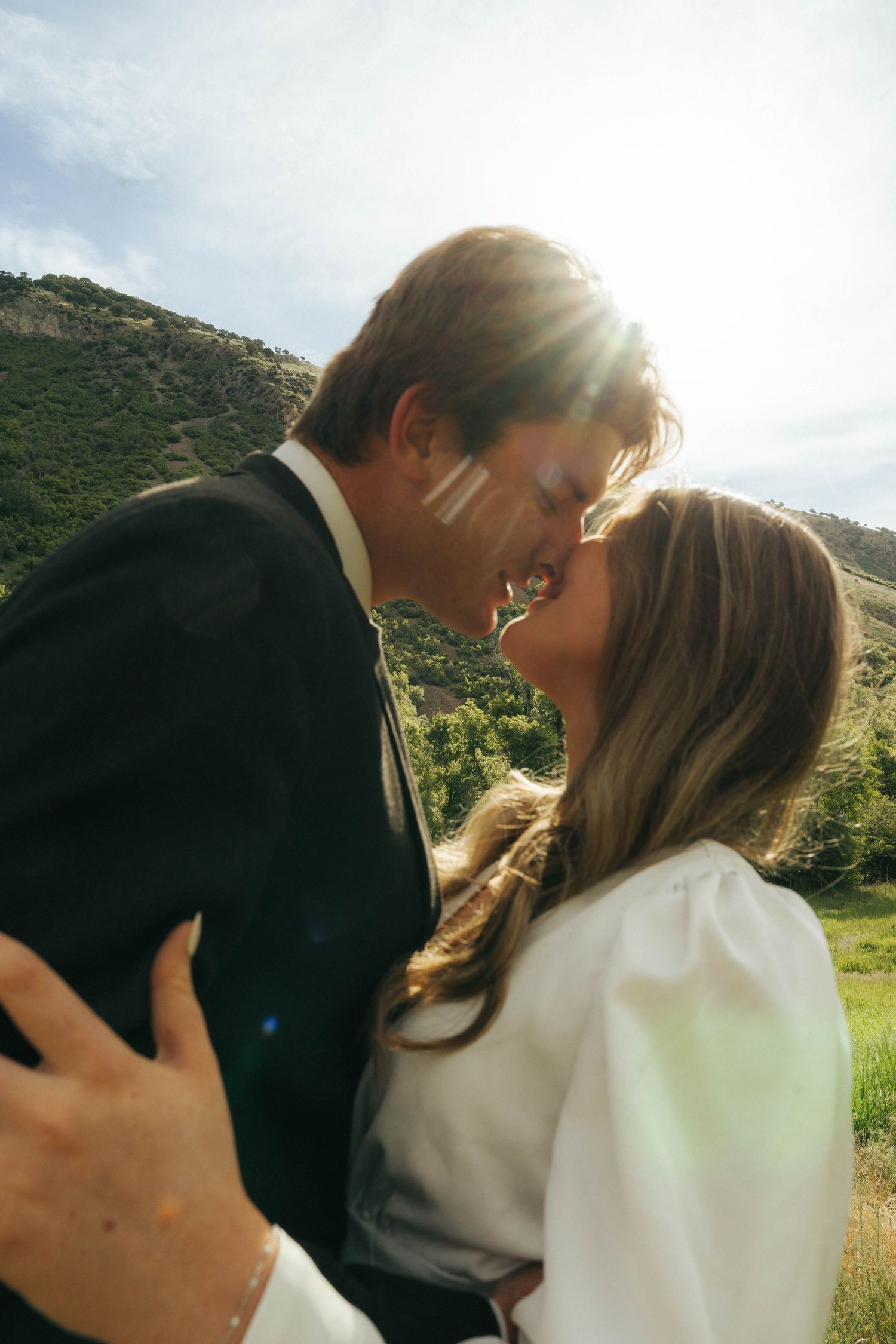 A romantic couple embracing in a sunlit mountain meadow during their engagement photoshoot.
