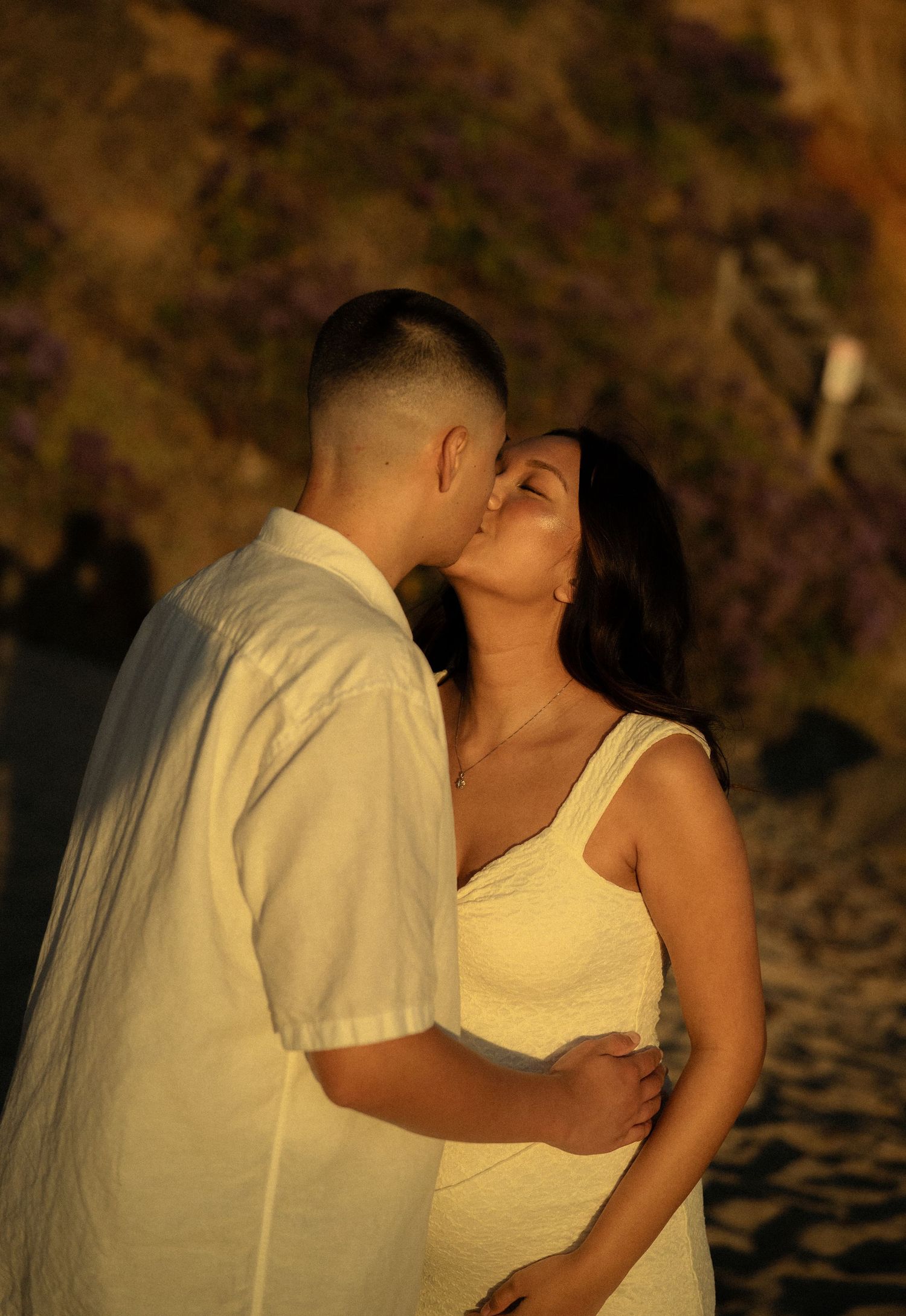 Couple sharing a tender kiss during golden hour with purple wildflowers in background.