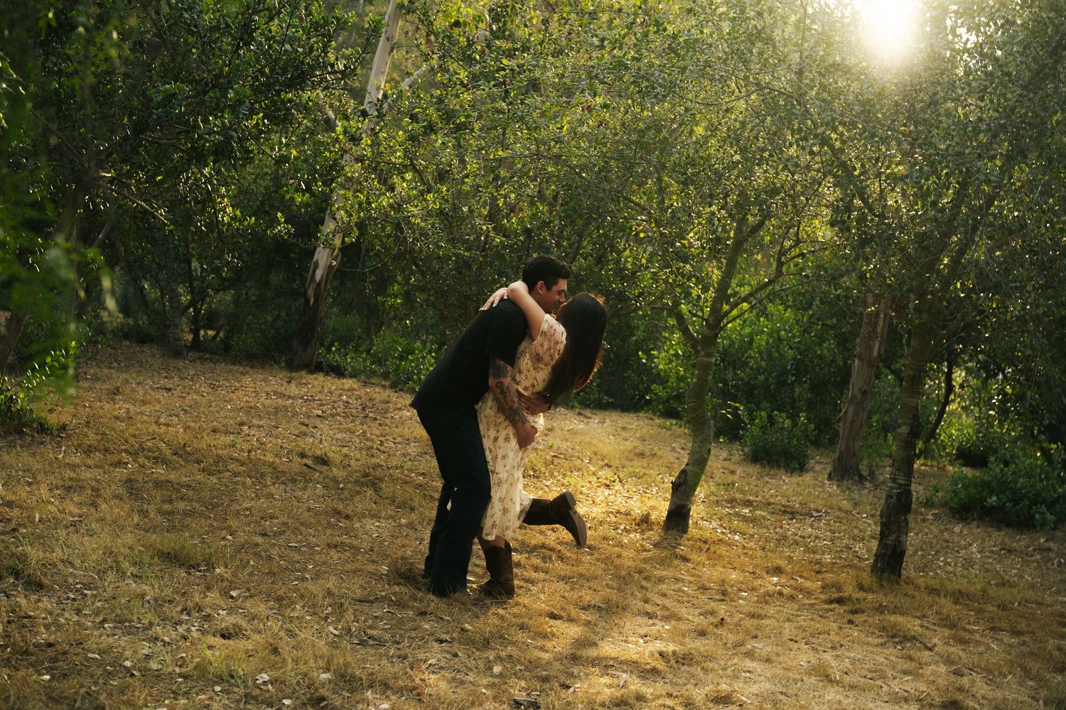 Couple embracing and dancing romantically in a sunlit forest clearing surrounded by lush green trees.