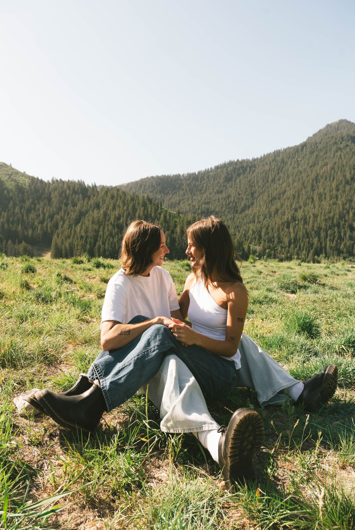 Two people relax together on a grassy hillside with mountain vistas in the distance.