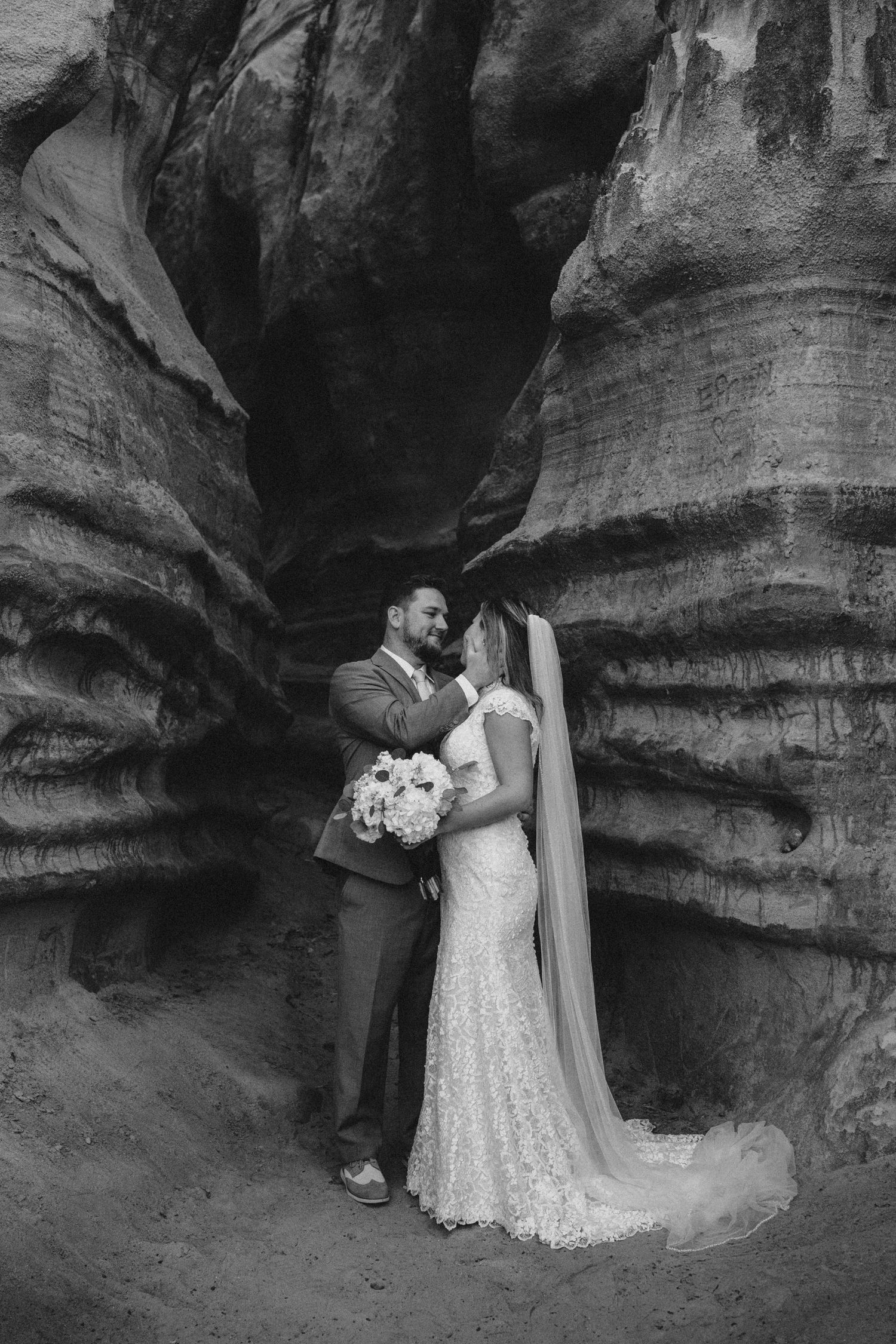 Black and white romantic wedding portrait of couple embracing in dramatic sandstone canyon with flowing veil.