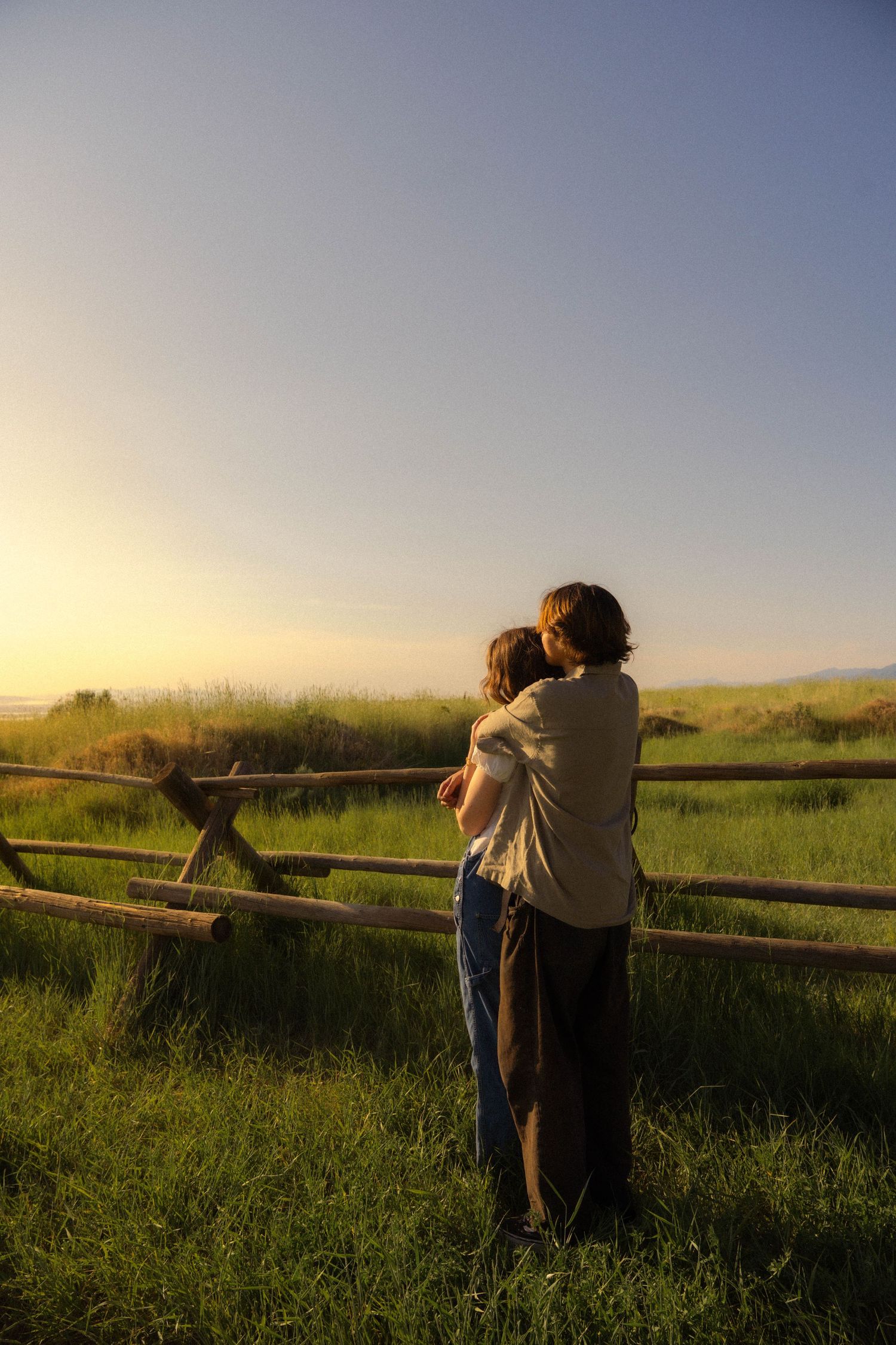 Couple sharing an intimate moment at sunset while leaning on a wooden fence.
