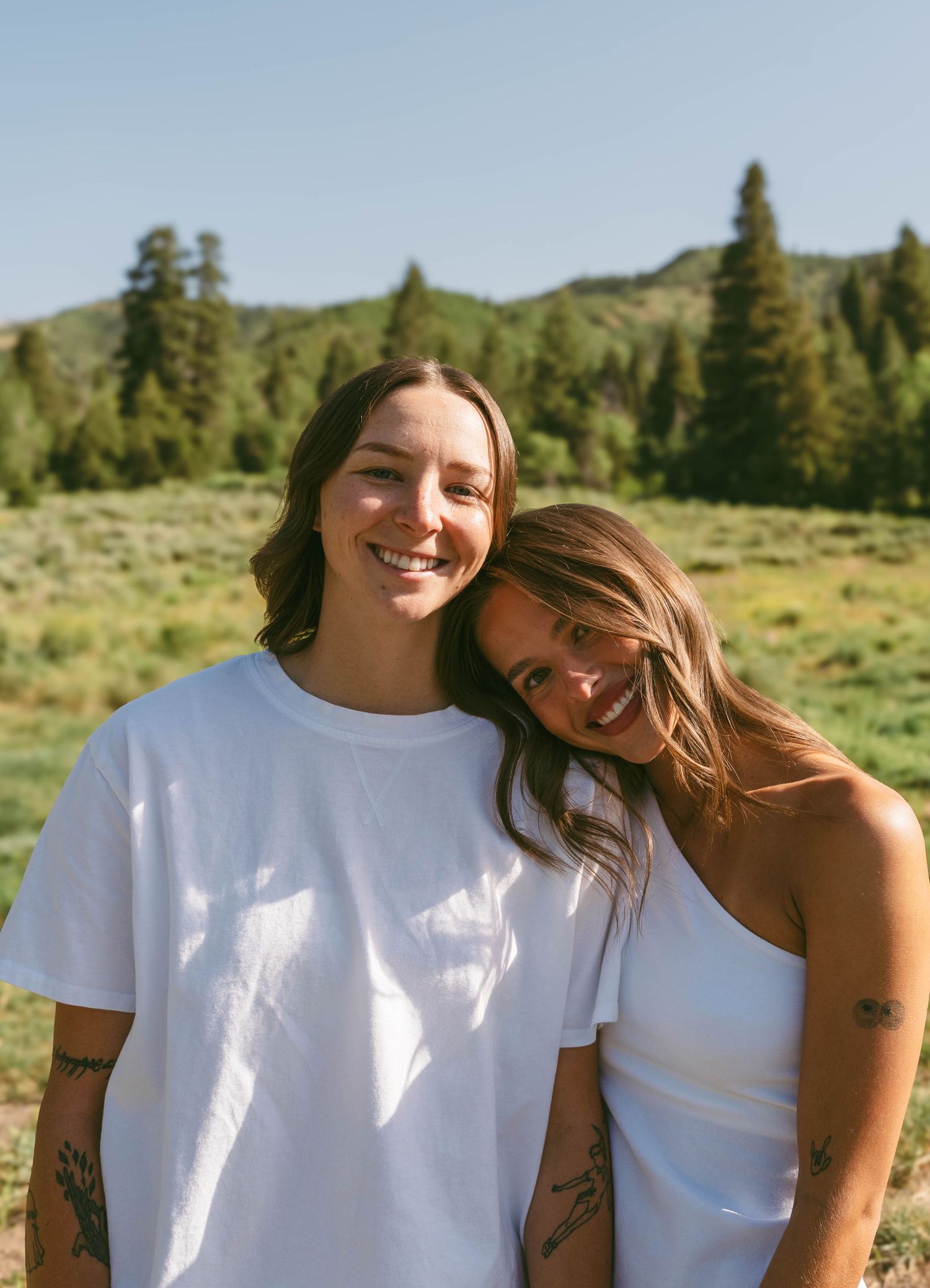 Two people in white tops smiling and embracing on a sunny mountain slope.