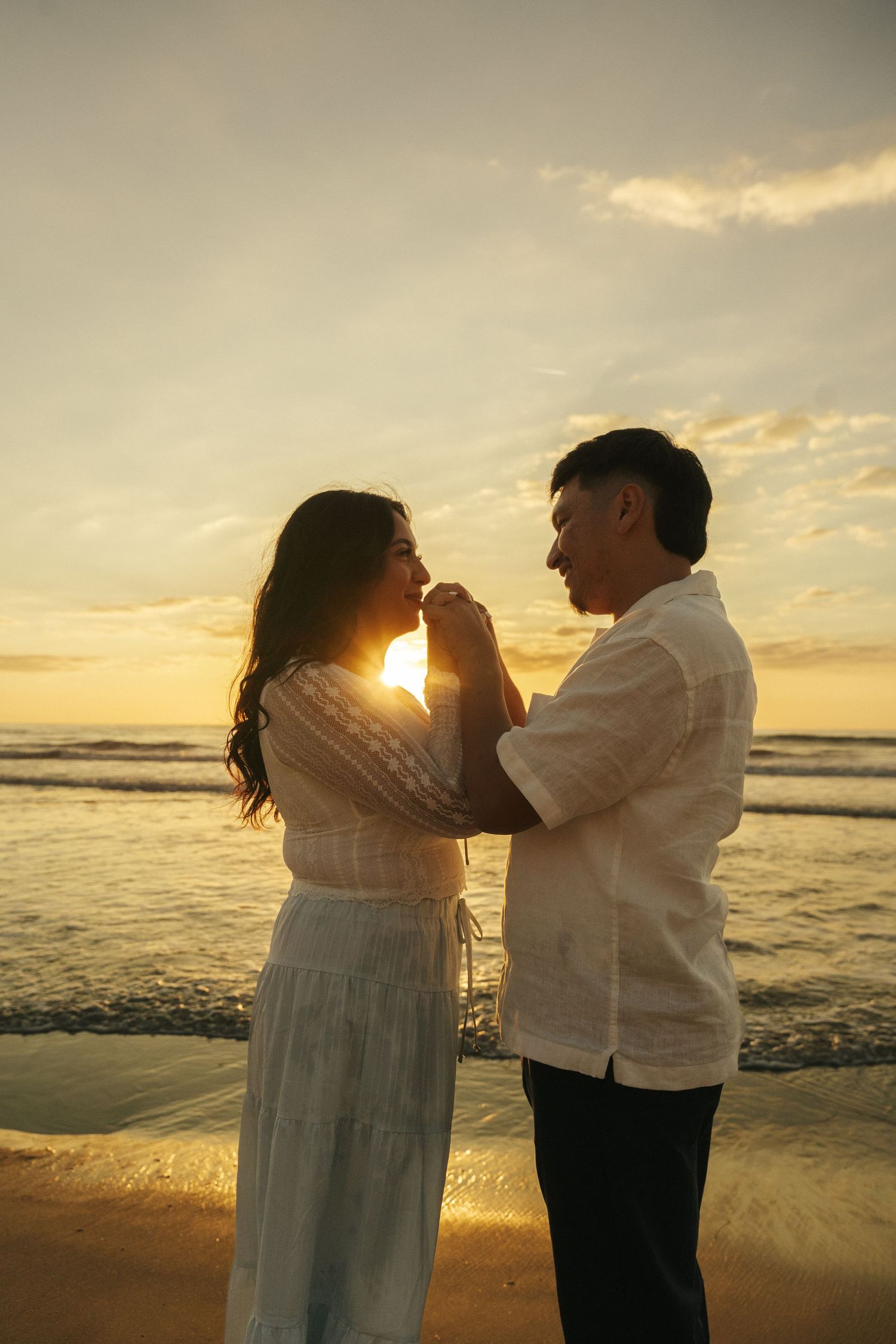 Intimate moment between couple on Southern California sandy beach with golden sunset behind them.