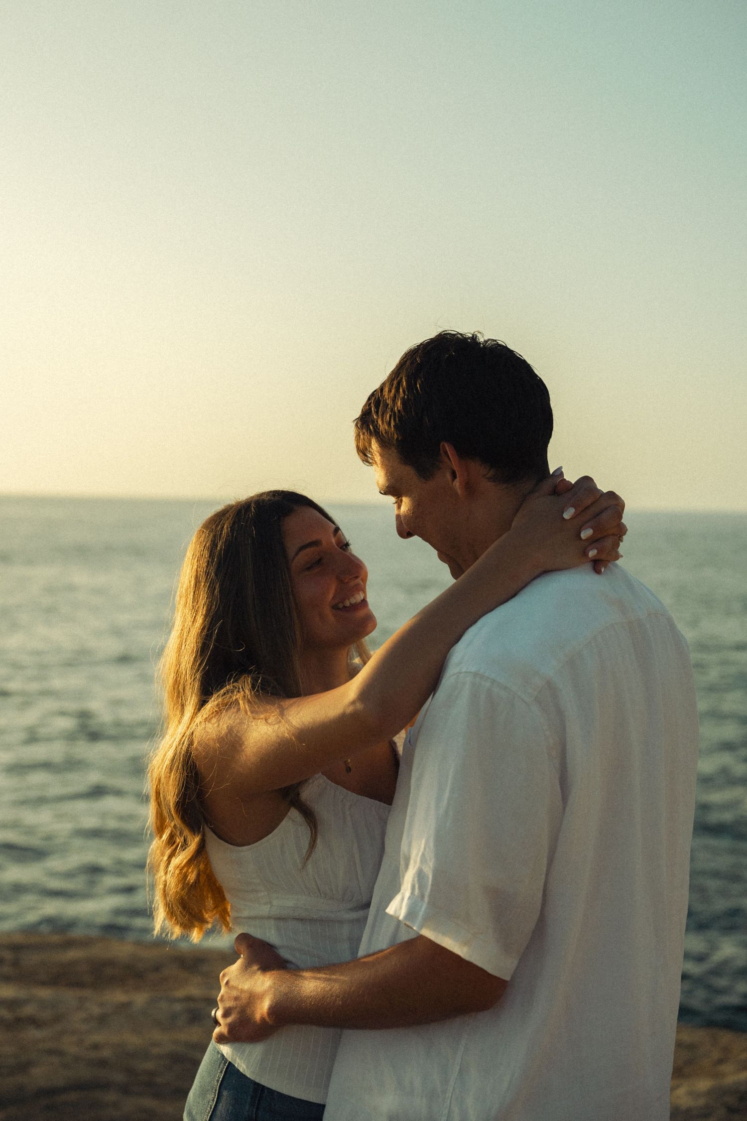 Happy couple embracing and smiling at sunset by the sea.