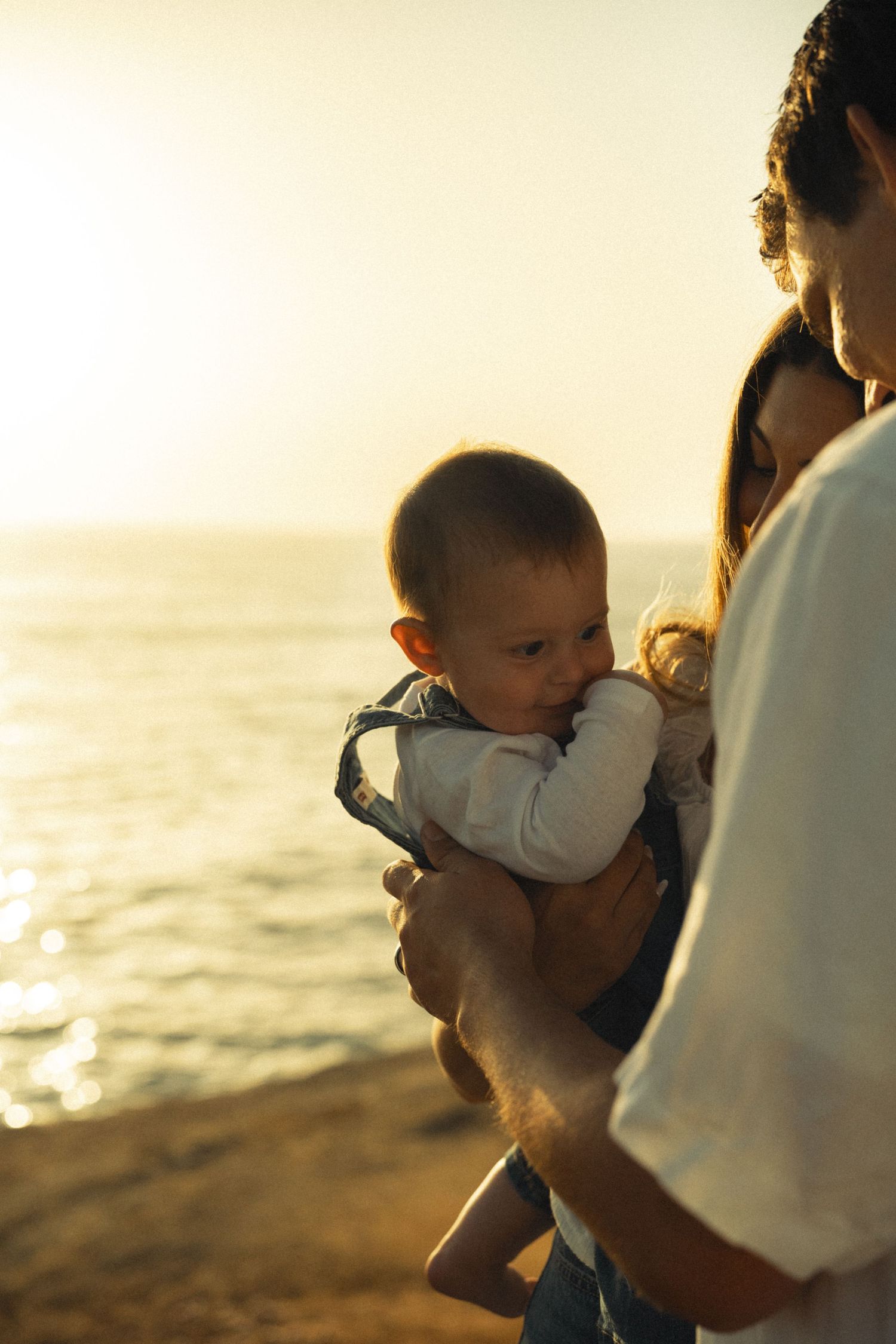 Parents holding their baby at golden hour by the ocean shore.