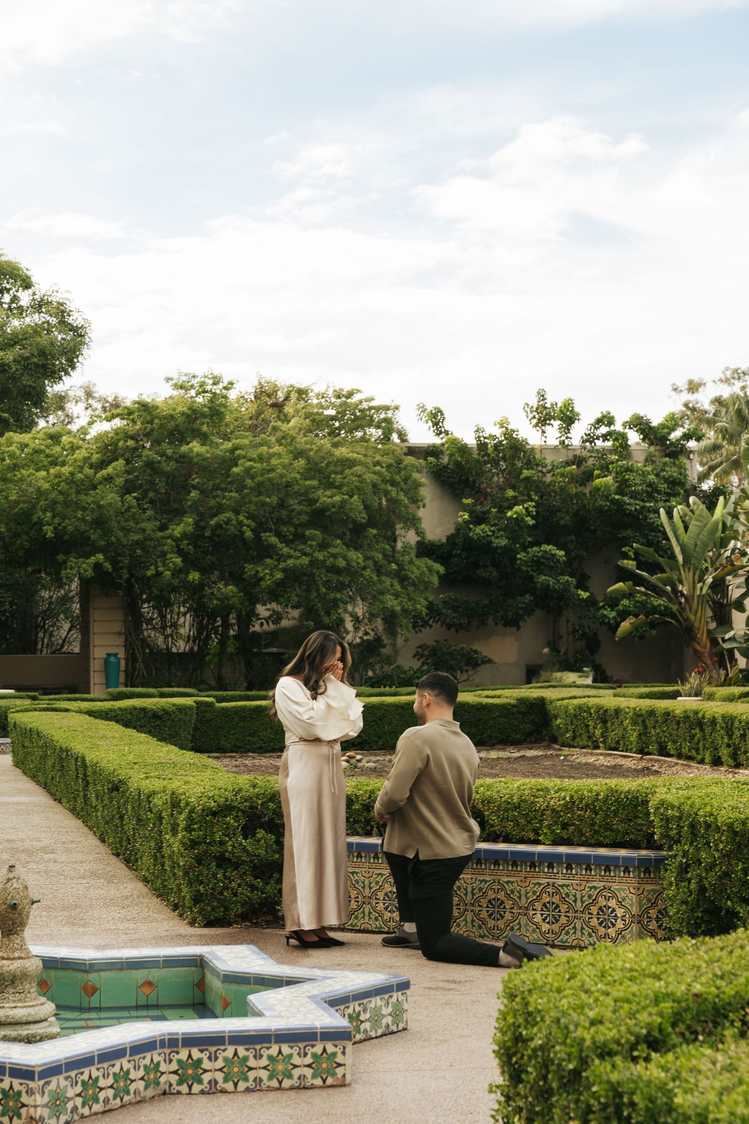 Two people sitting together on a decorative tiled bench in a peaceful garden setting at Balboa Park.
