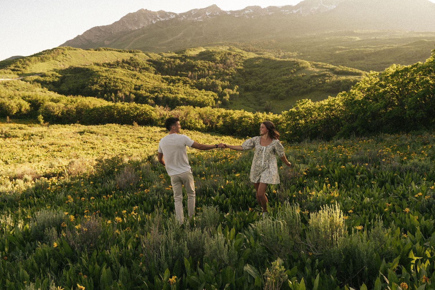 Two people walking through a mountainside meadow at golden hour.