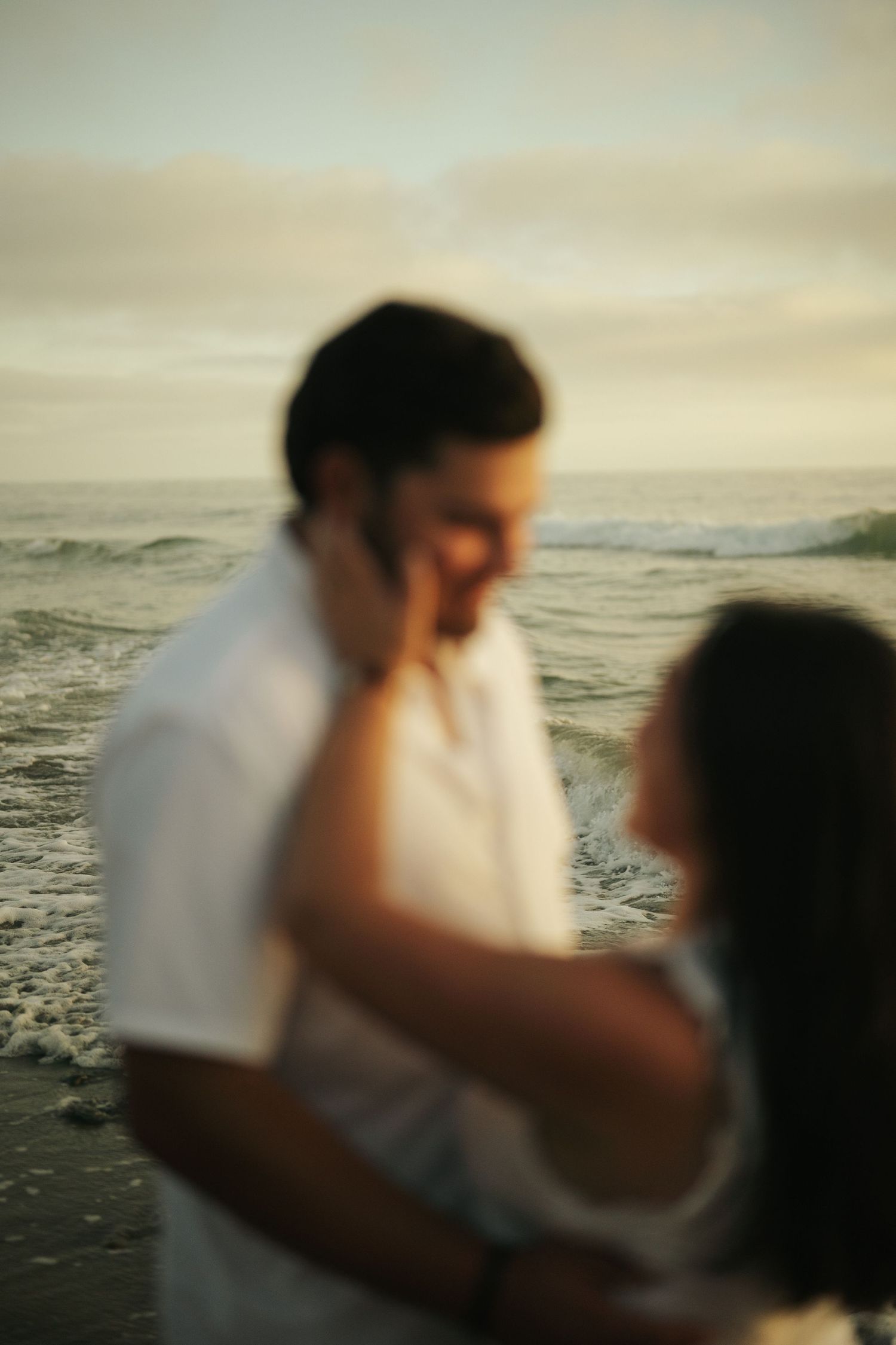 Blurry romantic couple embracing on a beach at sunset with ocean waves in the background.