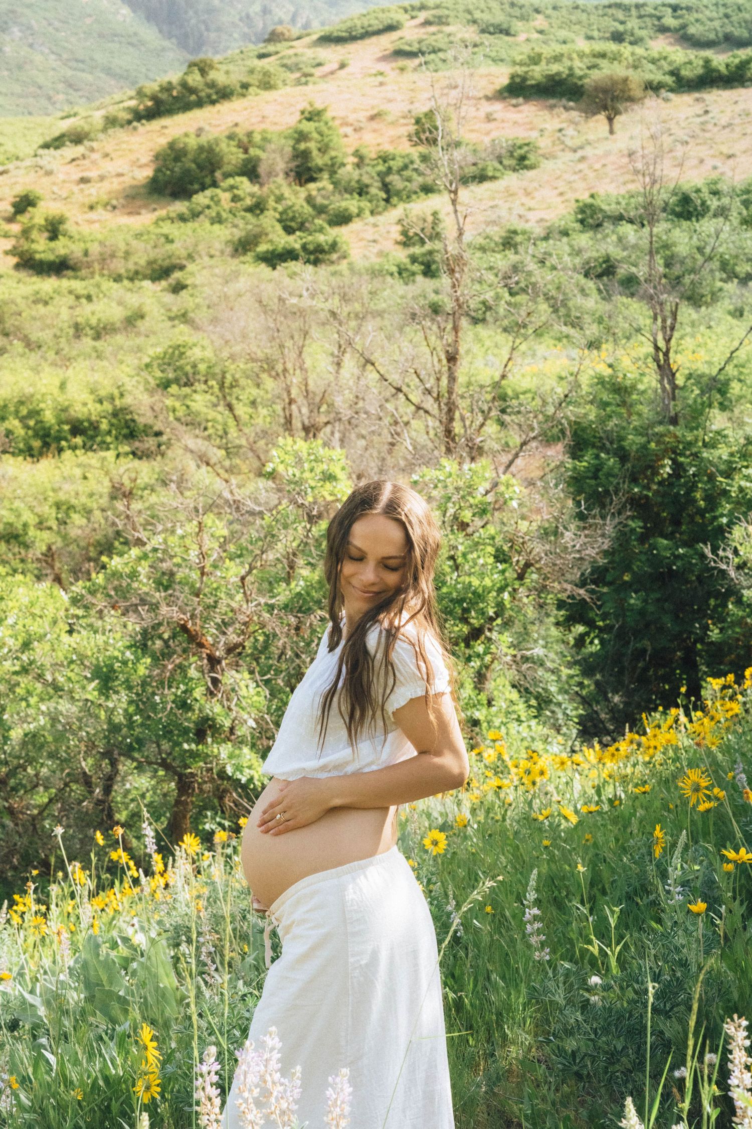 Dreamy maternity photos among yellow wildflowers on a hillside.