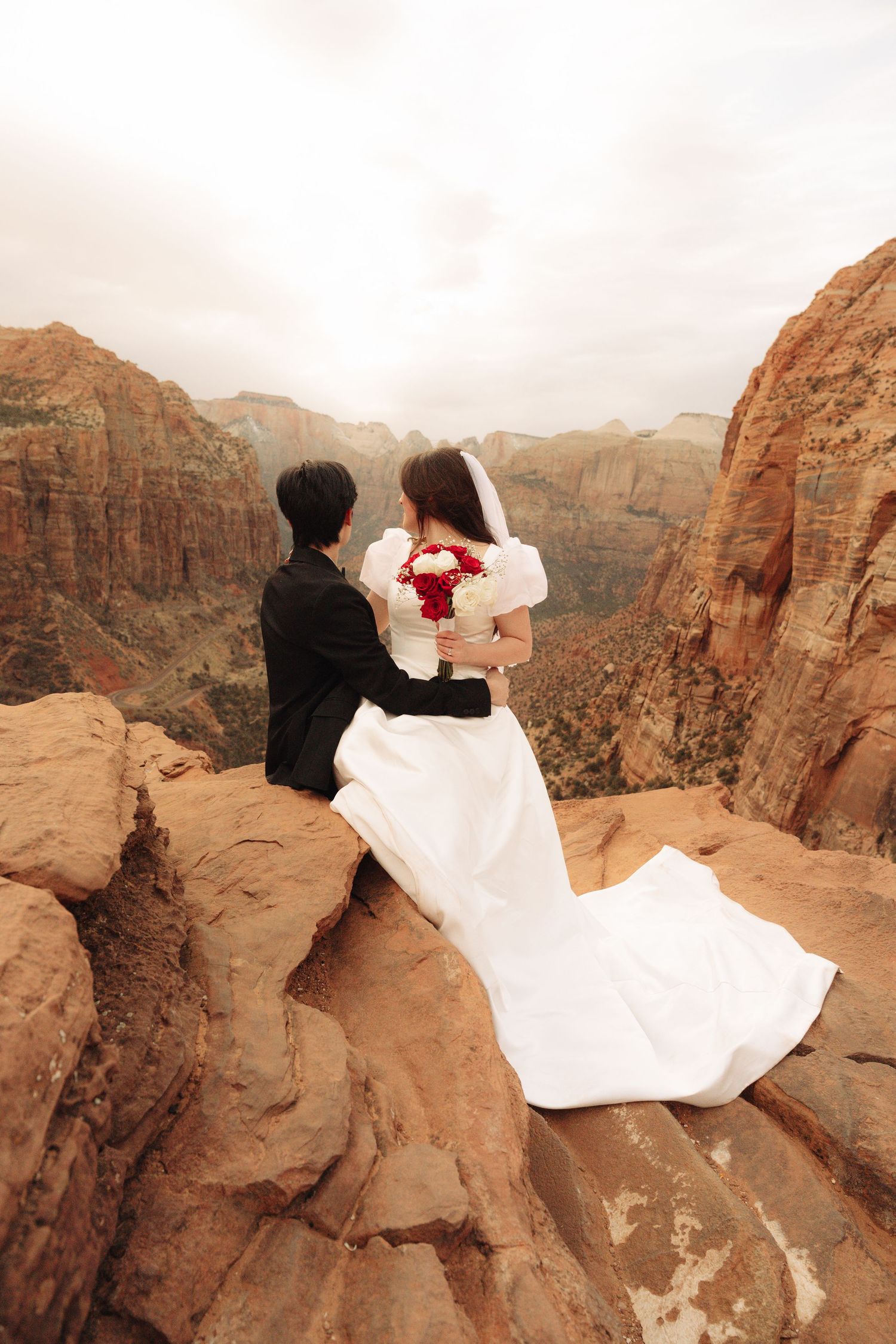 Wedding couple shares intimate moment atop dramatic red rock canyon cliffs.