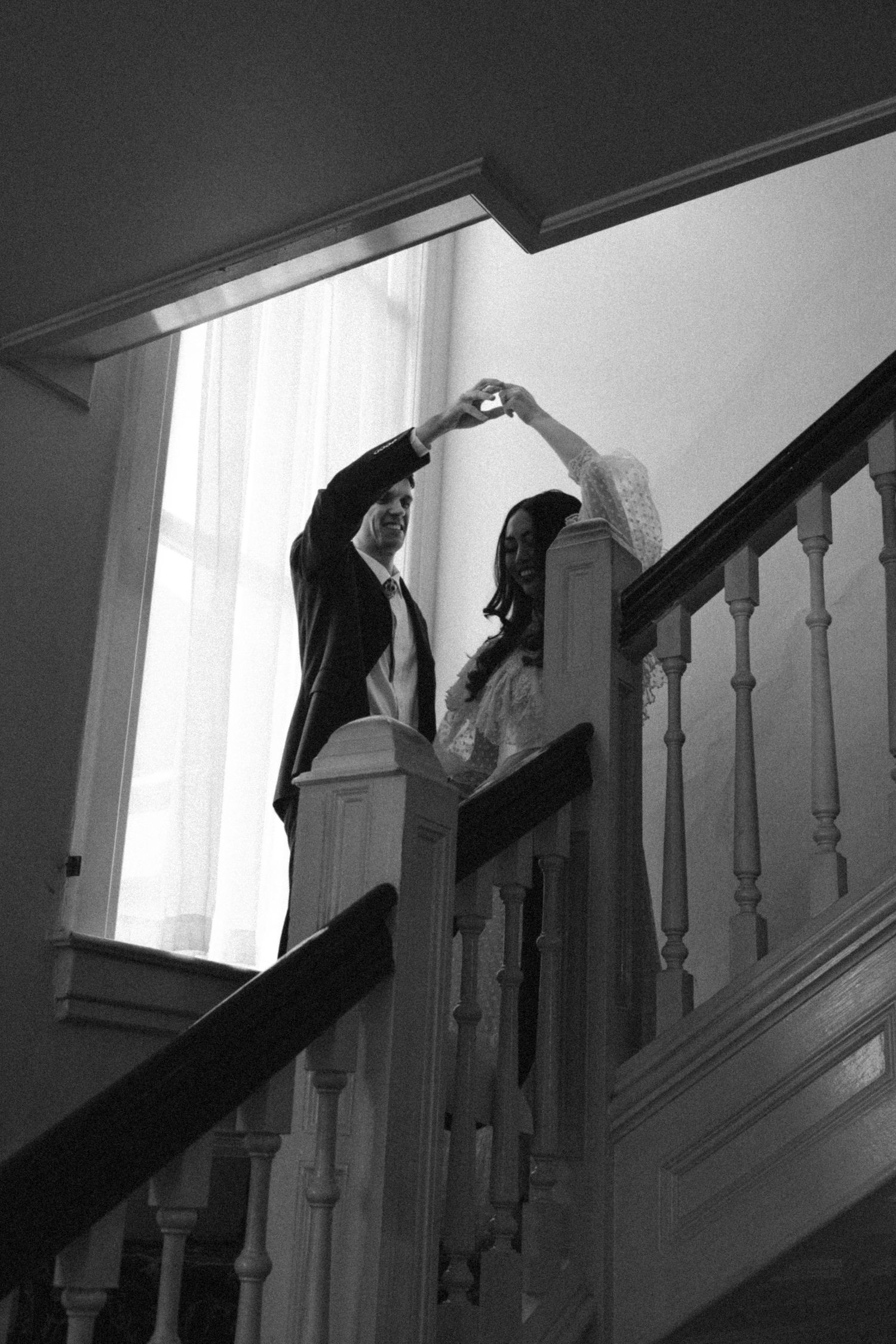 Black and white photo of a couple dancing on a staircase, forming a heart shape with their hands.