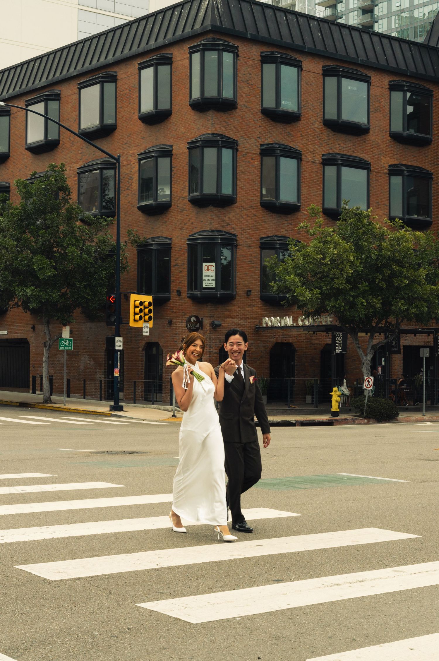 Bride and groom crossing a zebra crossing in front of a brick building on their wedding day.