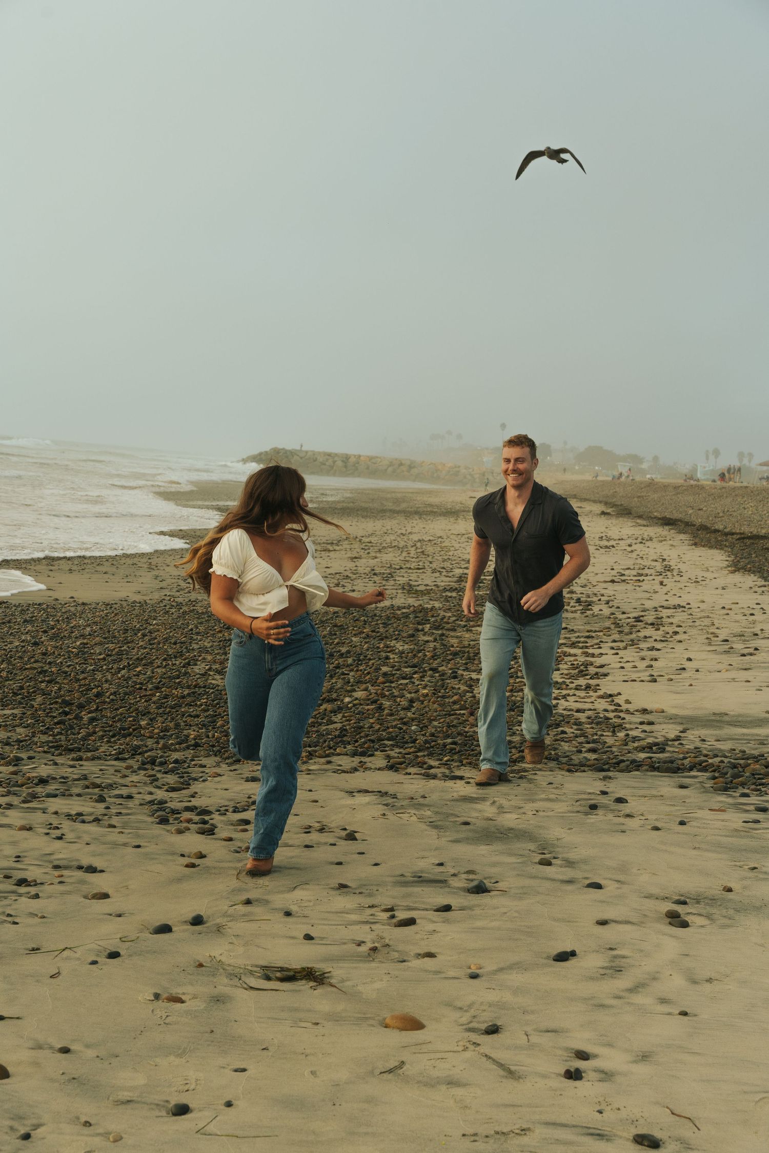 Friends playing and running on a rocky beach during an overcast day.
