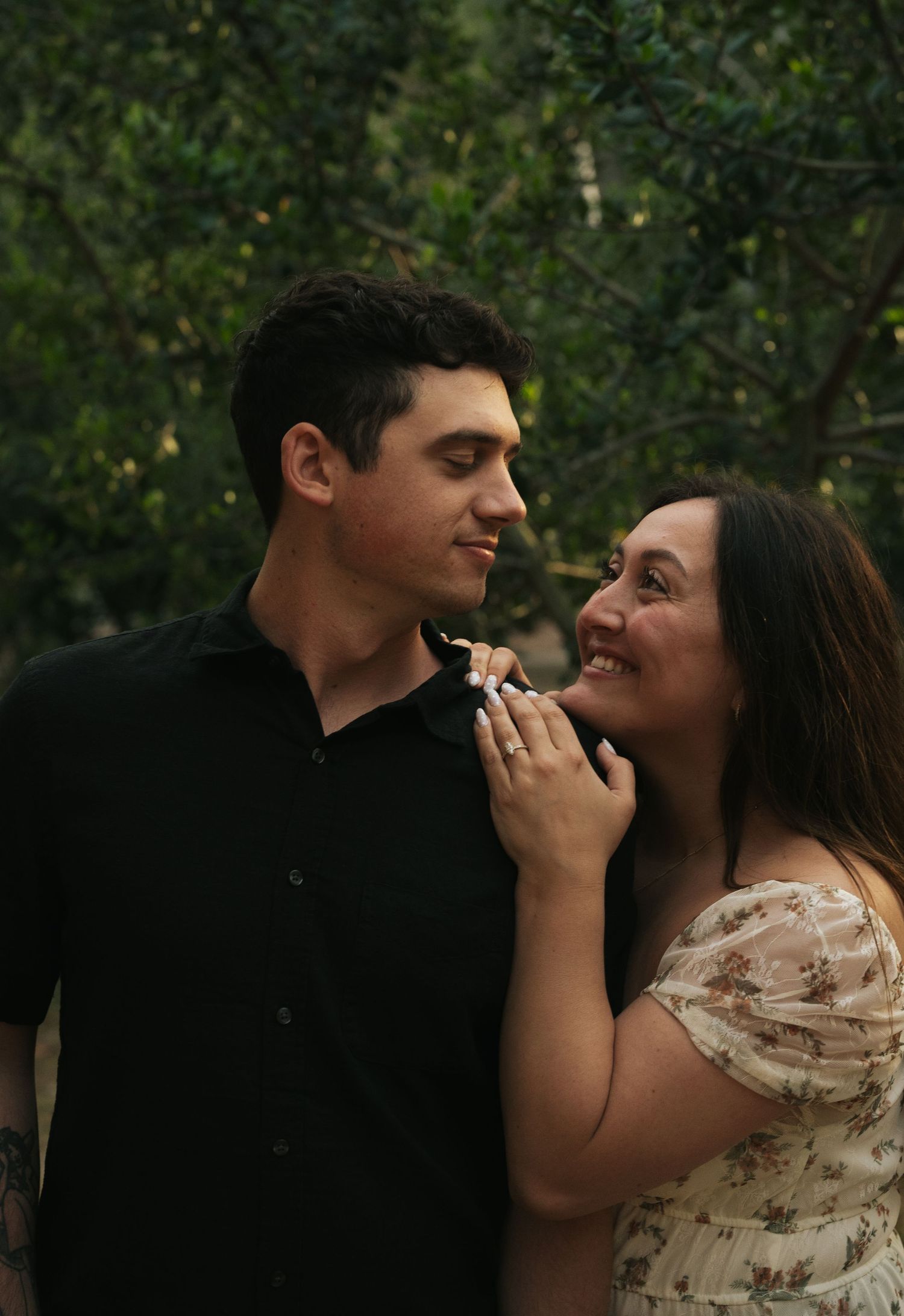 Smiling couple sharing a tender moment outdoors with green foliage in the background.
