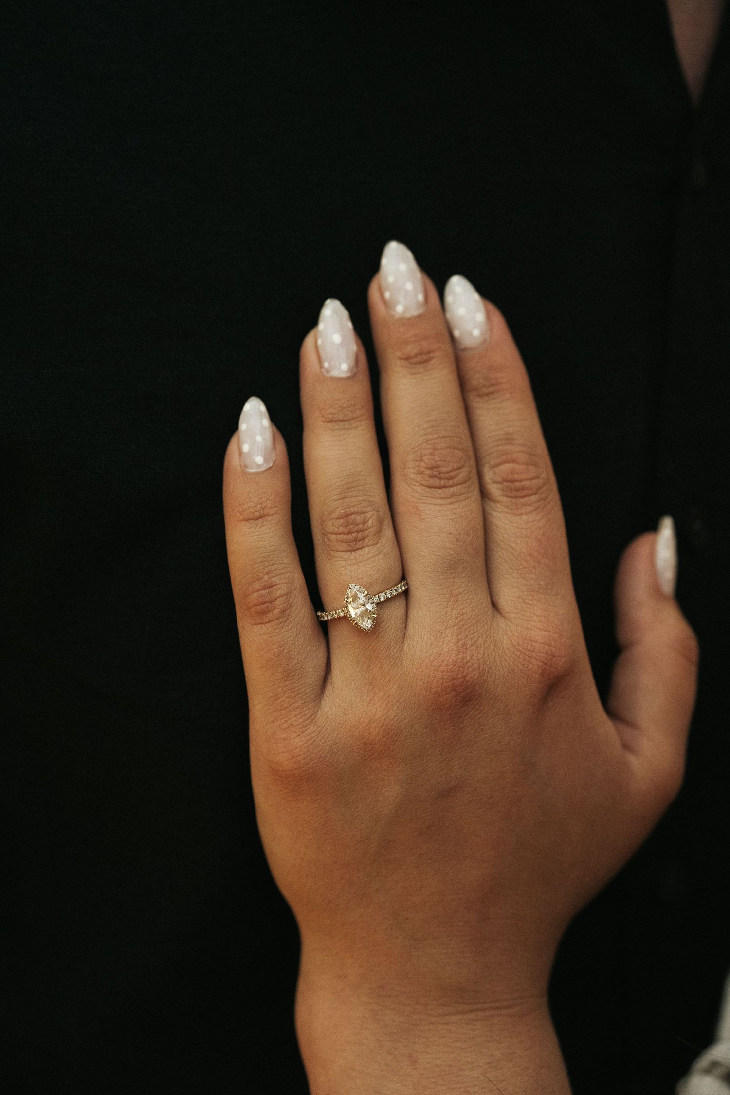Close-up of an engagement ring with marquise diamond on a hand with white manicured nails.