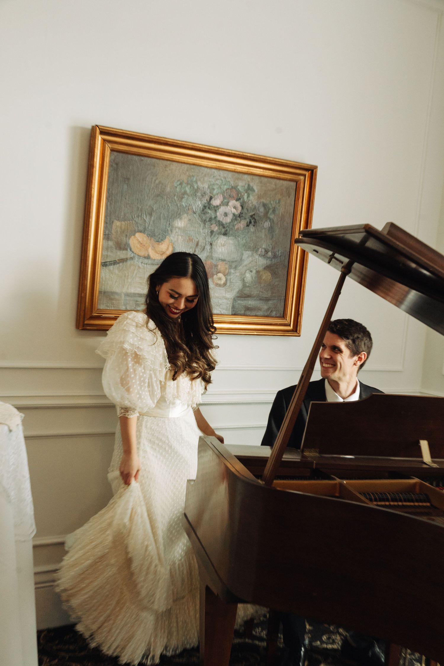 A romantic scene with a white lace dress and grand piano in an elegant room with framed artwork.