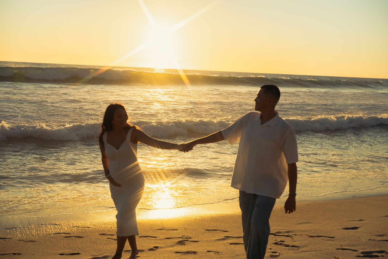 Happy couple holding hands strolling on a beach during a beautiful golden sunset.