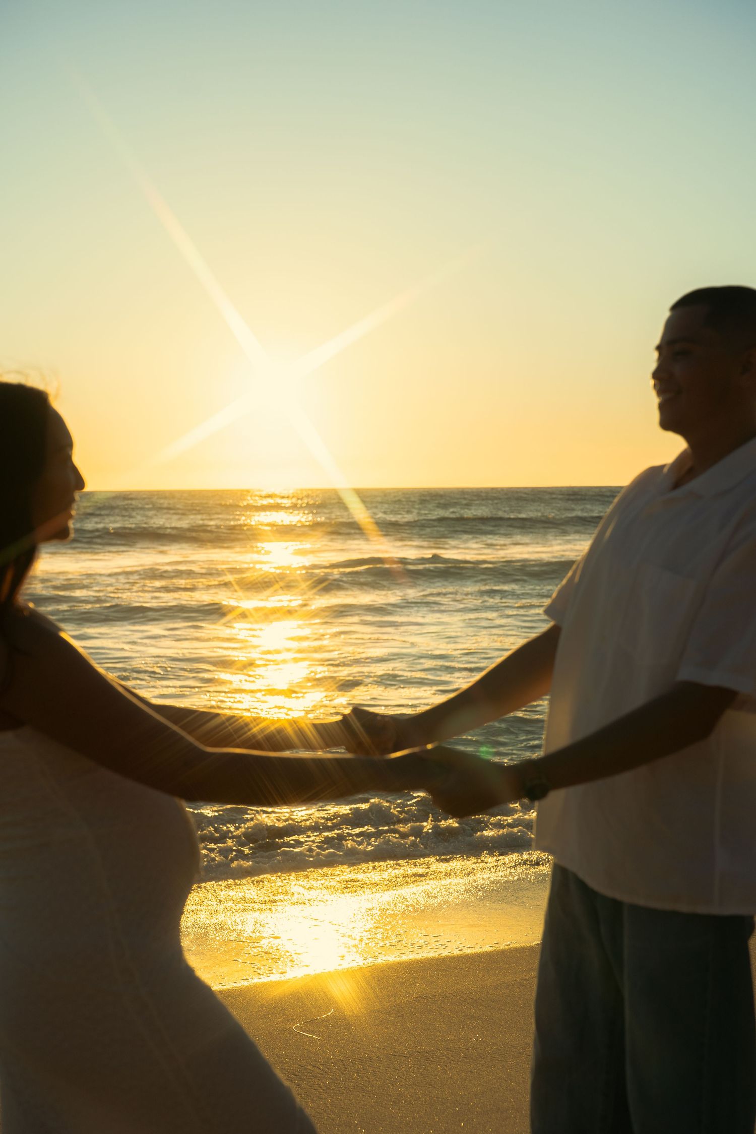 Romantic couple holding hands on a beach at golden sunset with ocean waves.