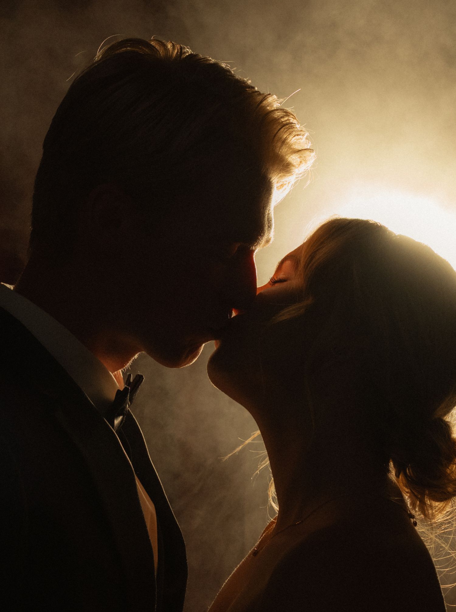 Romantic silhouette of a couple sharing a passionate kiss backlit by warm golden light.