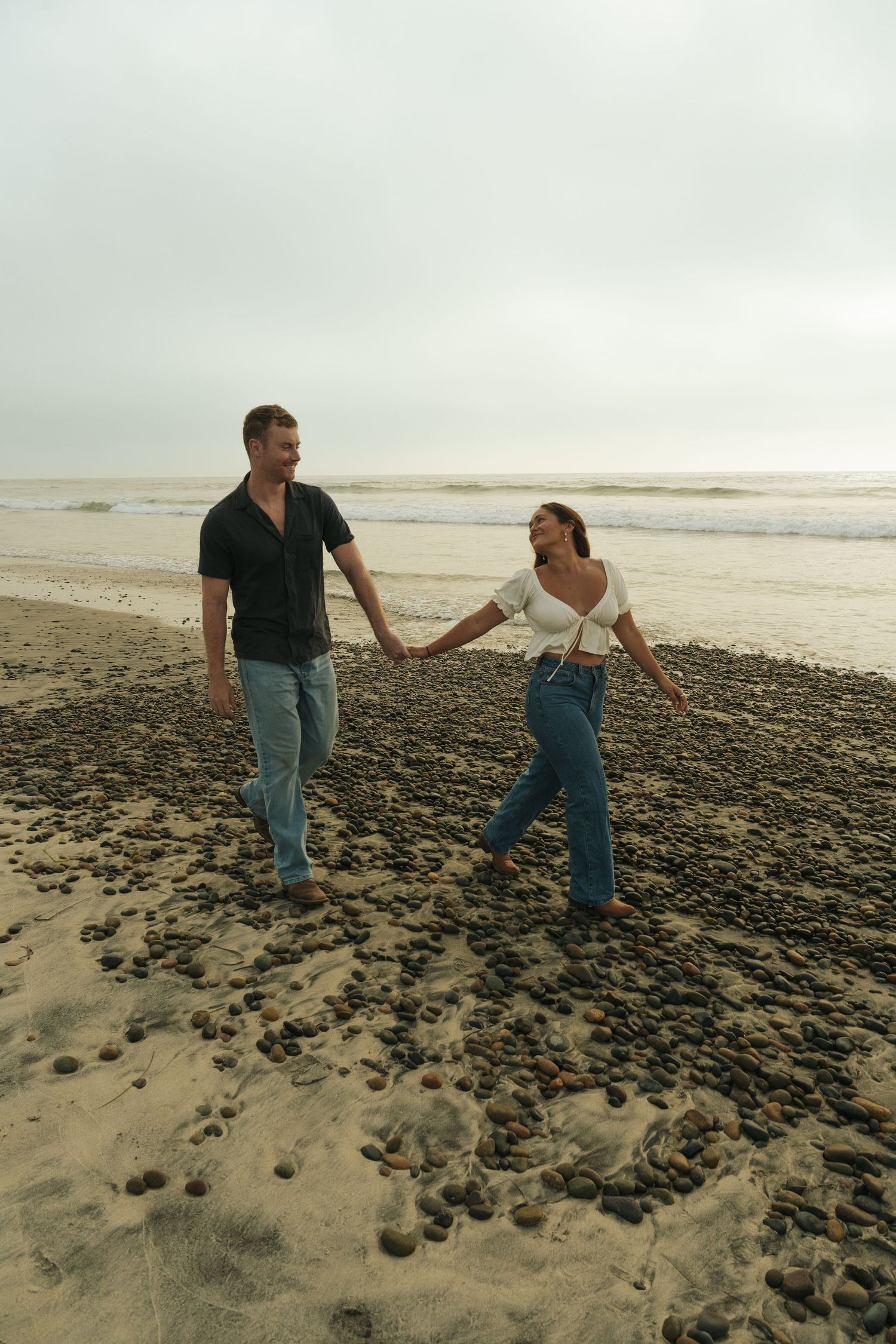 A couple walking together on a rocky beach shoreline in San Diego during an overcast day.
