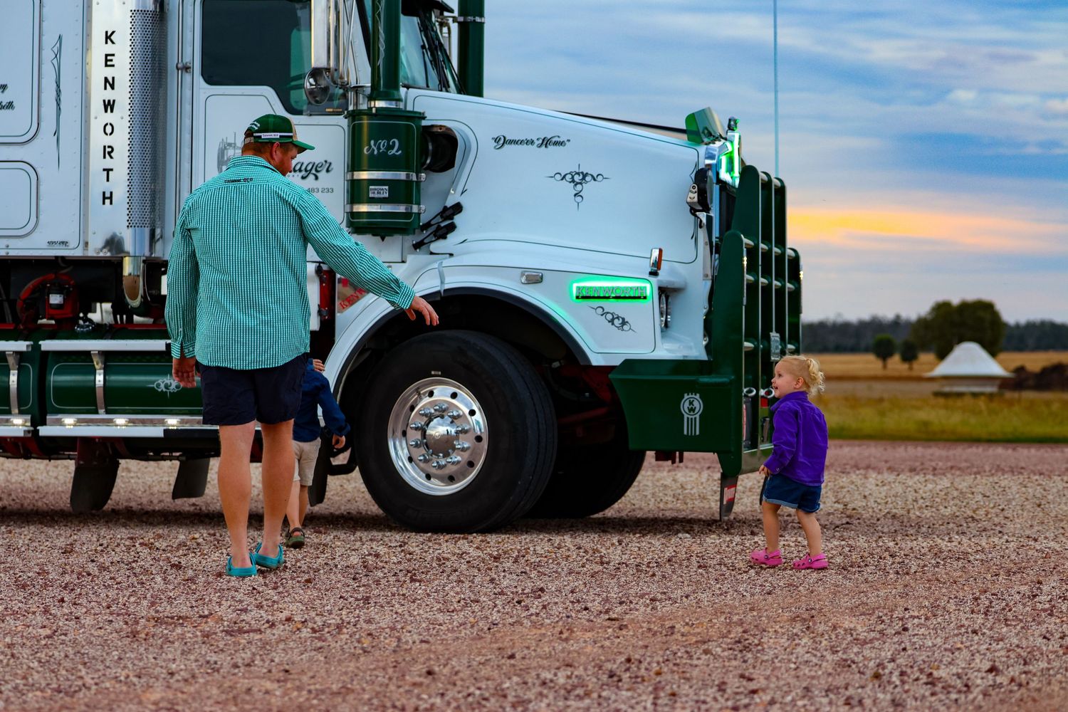 Waste management truck workers collect garbage bins on a residential street during sunrise.