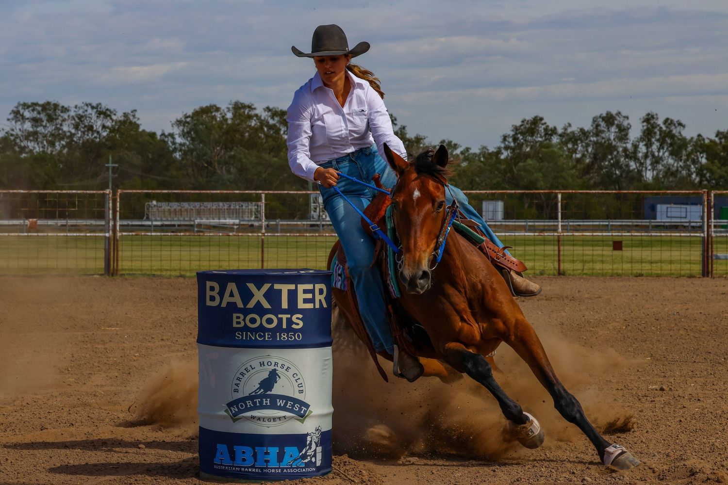 Barrel racing competitor on horseback makes a sharp turn around a barrel in a dusty rodeo arena during competition.