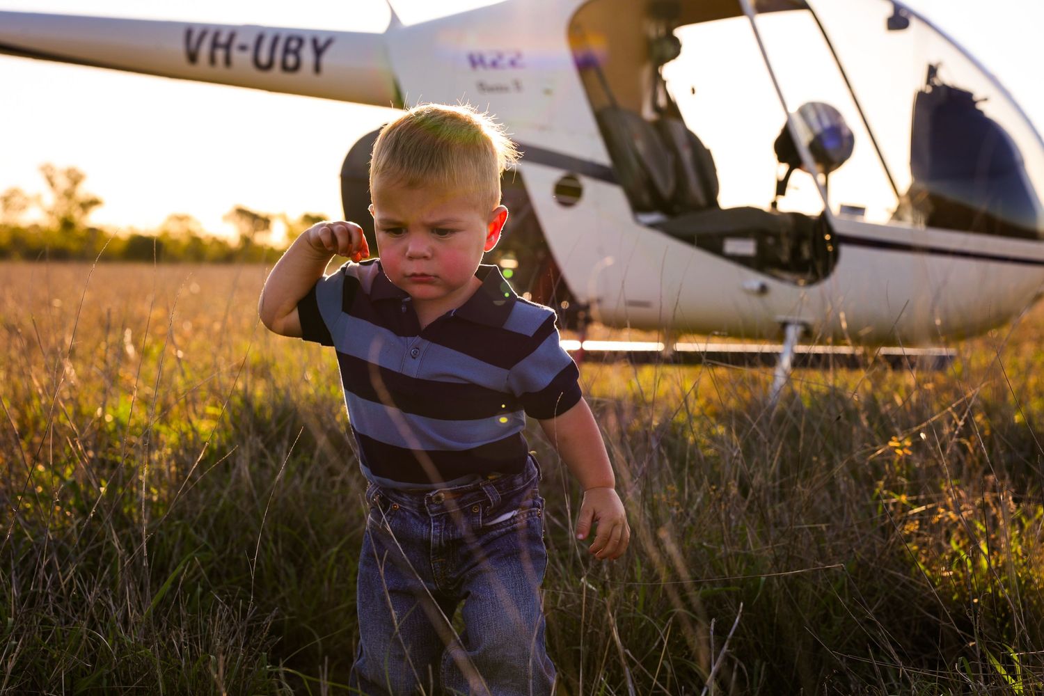 A small figure stands in a golden field at sunset with a light aircraft visible in the background.