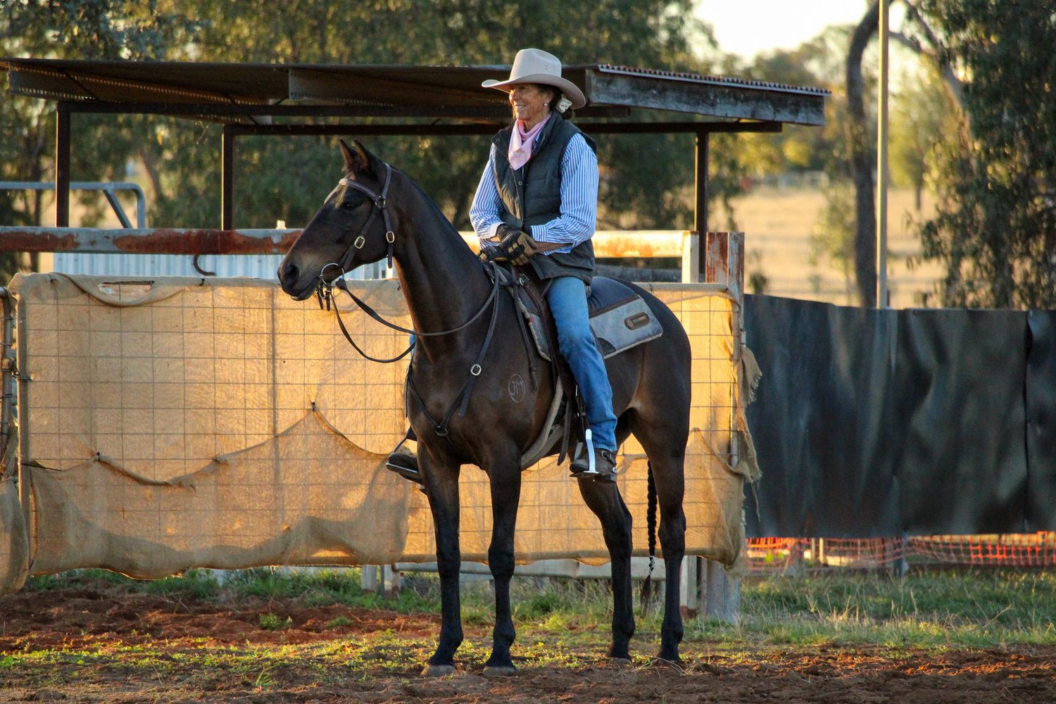 Western riders practicing near fence line during golden hour at training arena.