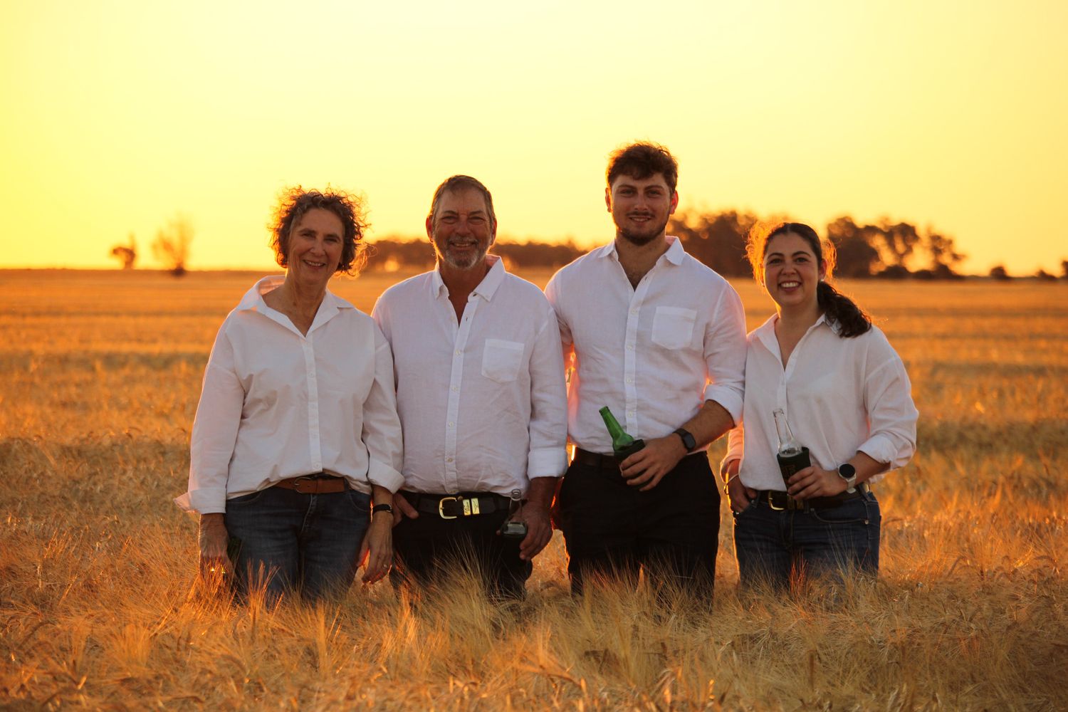 Group in white shirts laughing together while sitting in a golden wheat field at sunset.