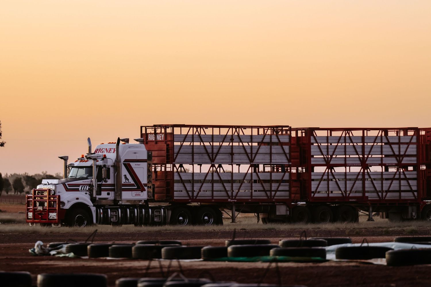 Silhouettes of industrial cranes and shipping containers against a vibrant orange sunset sky at a busy port terminal.