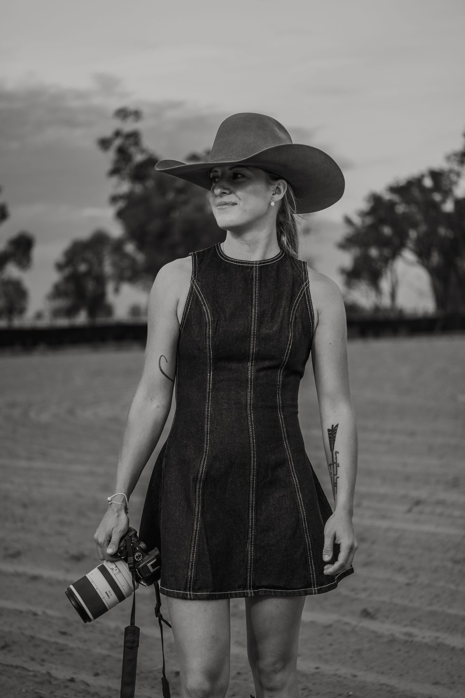A black and white photo series shows someone in a dark sleeveless top holding a camera in a rural field setting.