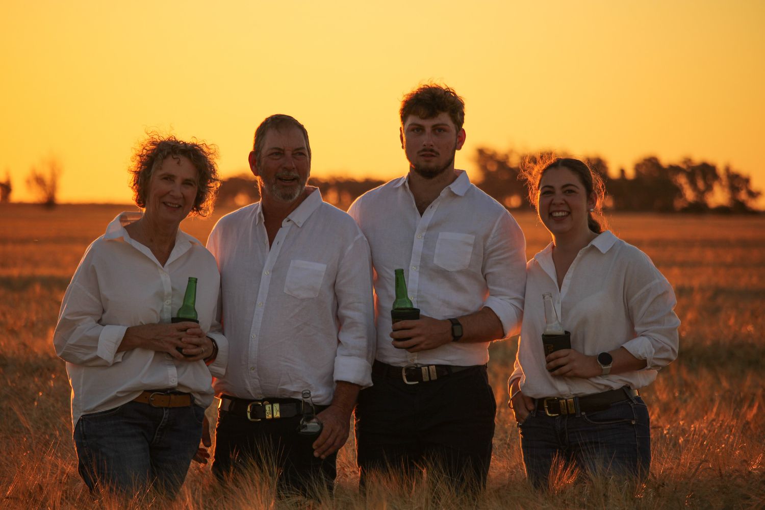 A group of people in white shirts stand together in a golden field at sunset.