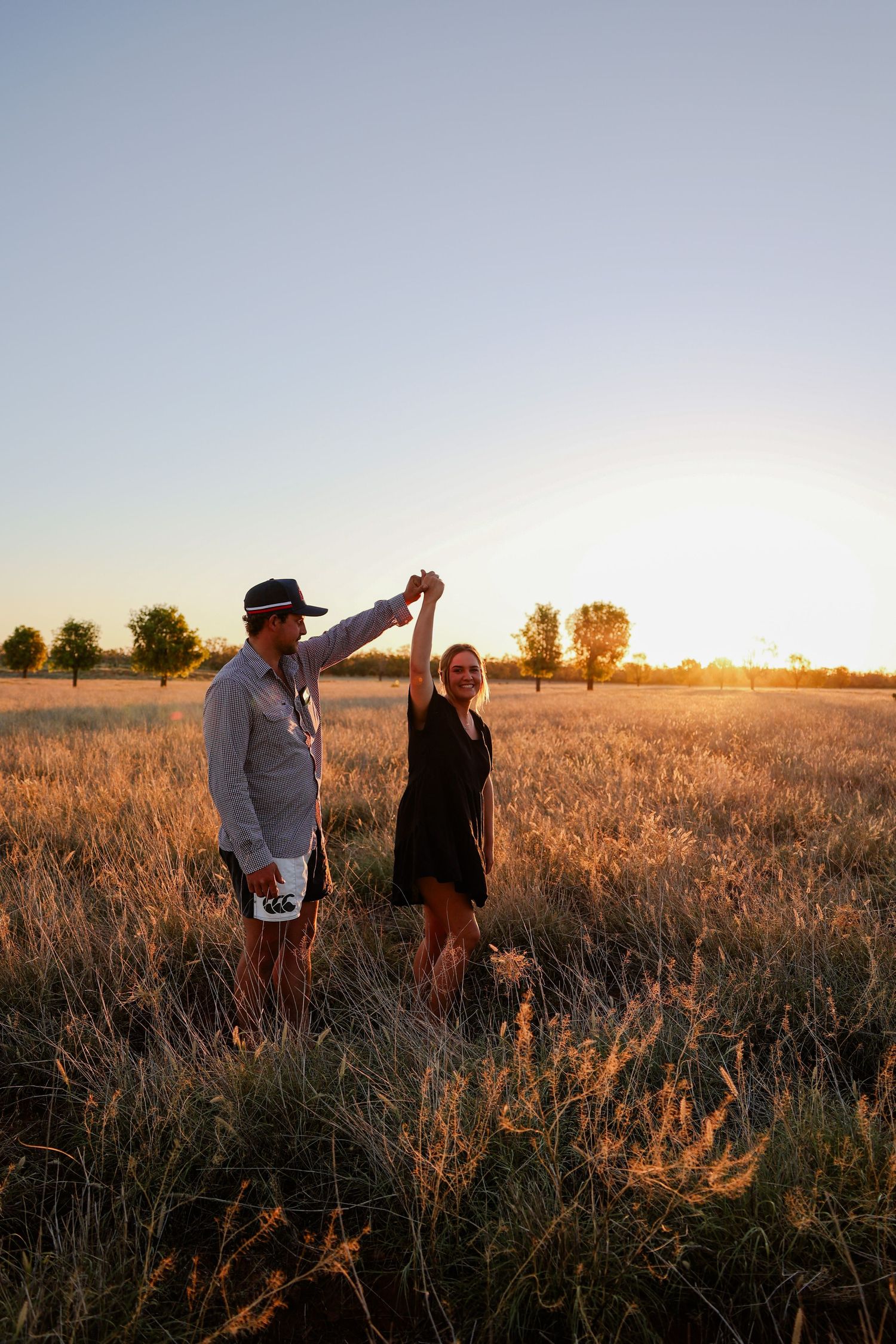 Two people walking together through a golden wheat field at sunset casting long shadows across the landscape.