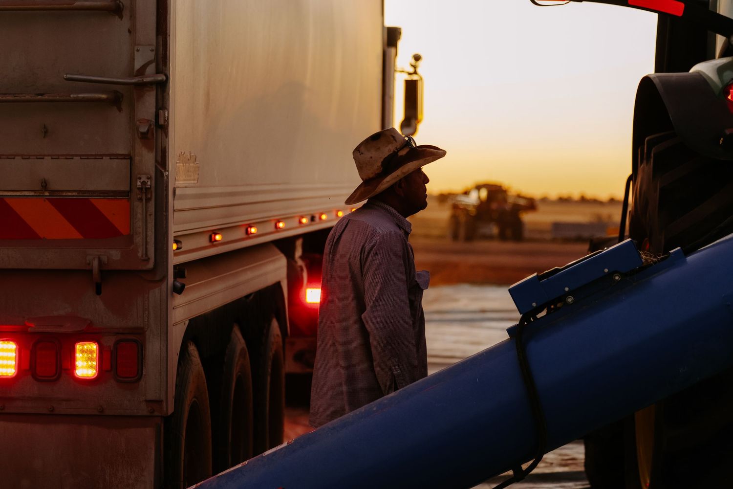 A silhouetted person in a cowboy hat stands beside a truck trailer at sunset, creating a dramatic western scene.