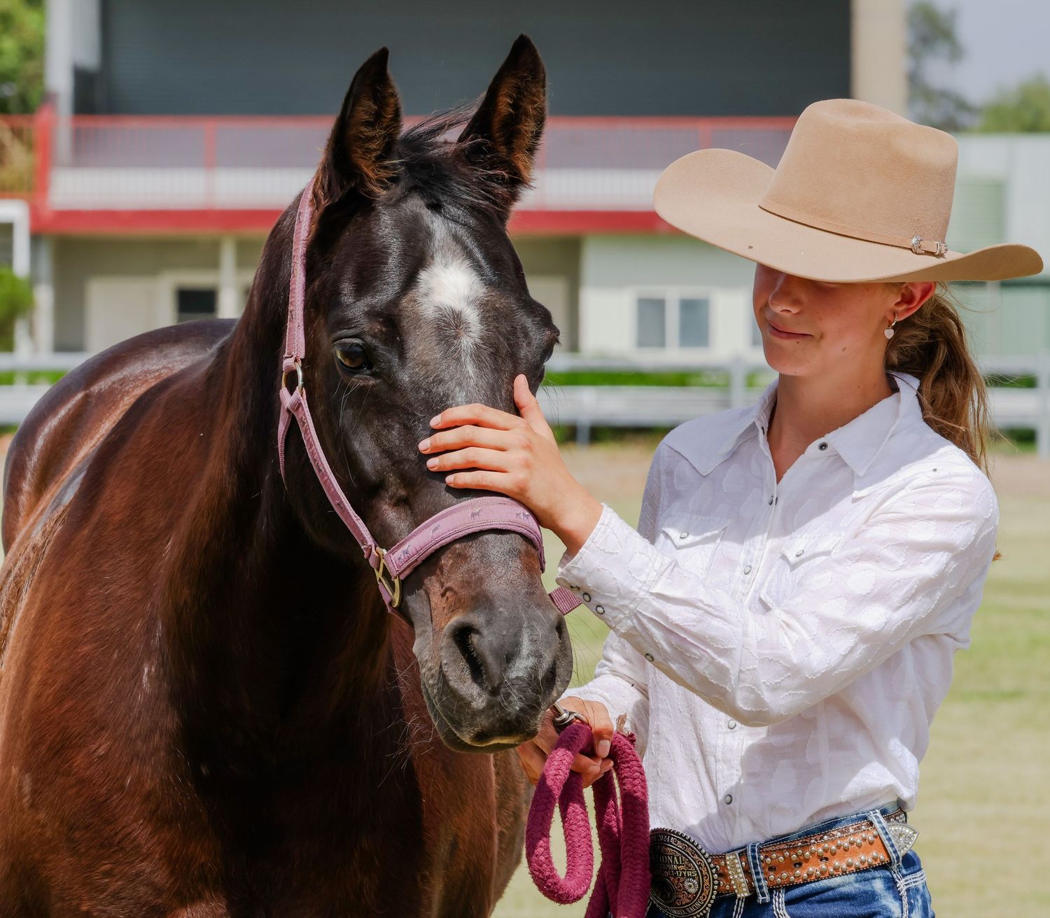 A brown horse and rider in western attire share a tender moment at an outdoor equestrian event.