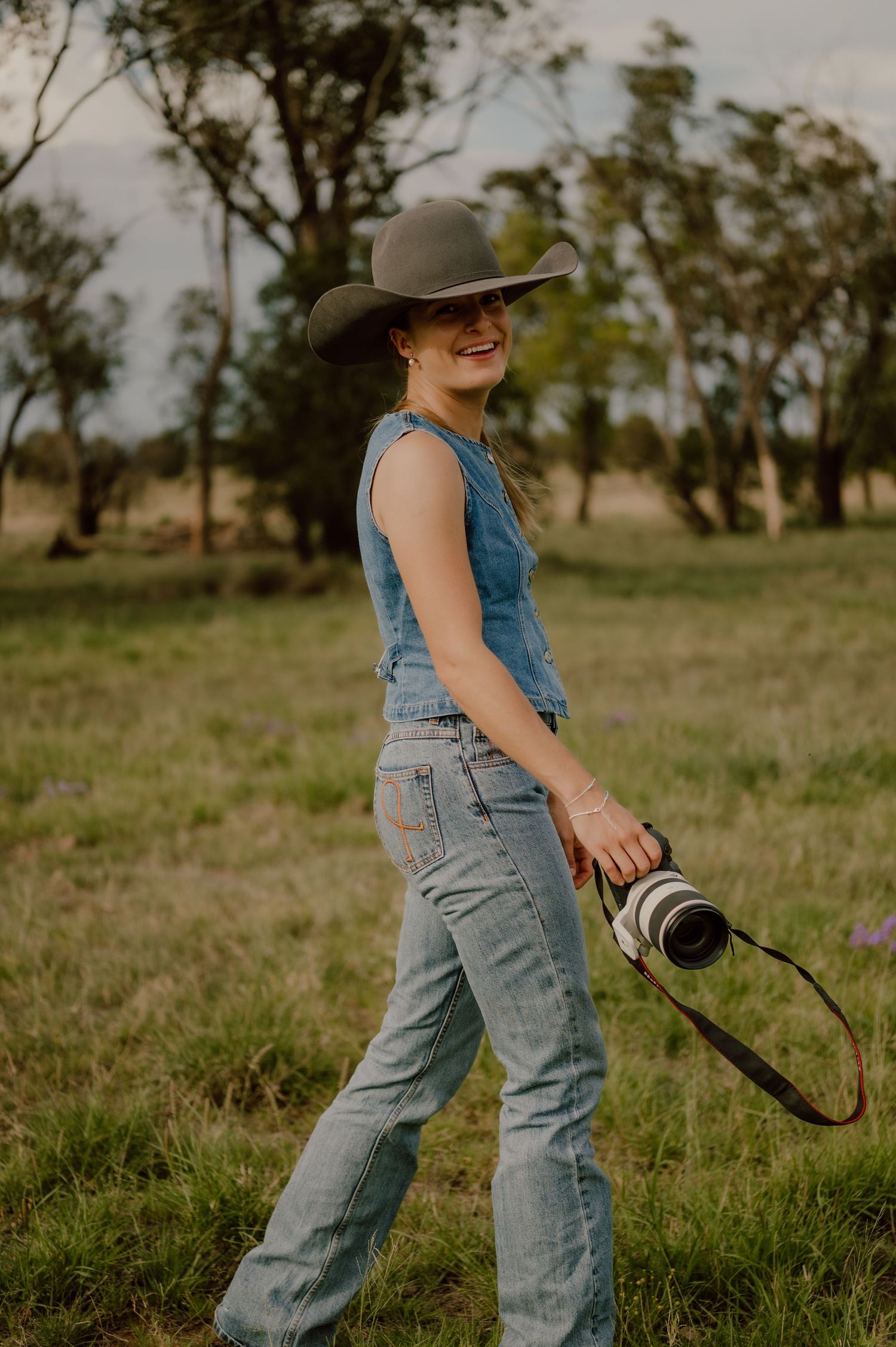 A person in denim overalls plays joyfully in a grassy field on a sunny afternoon.