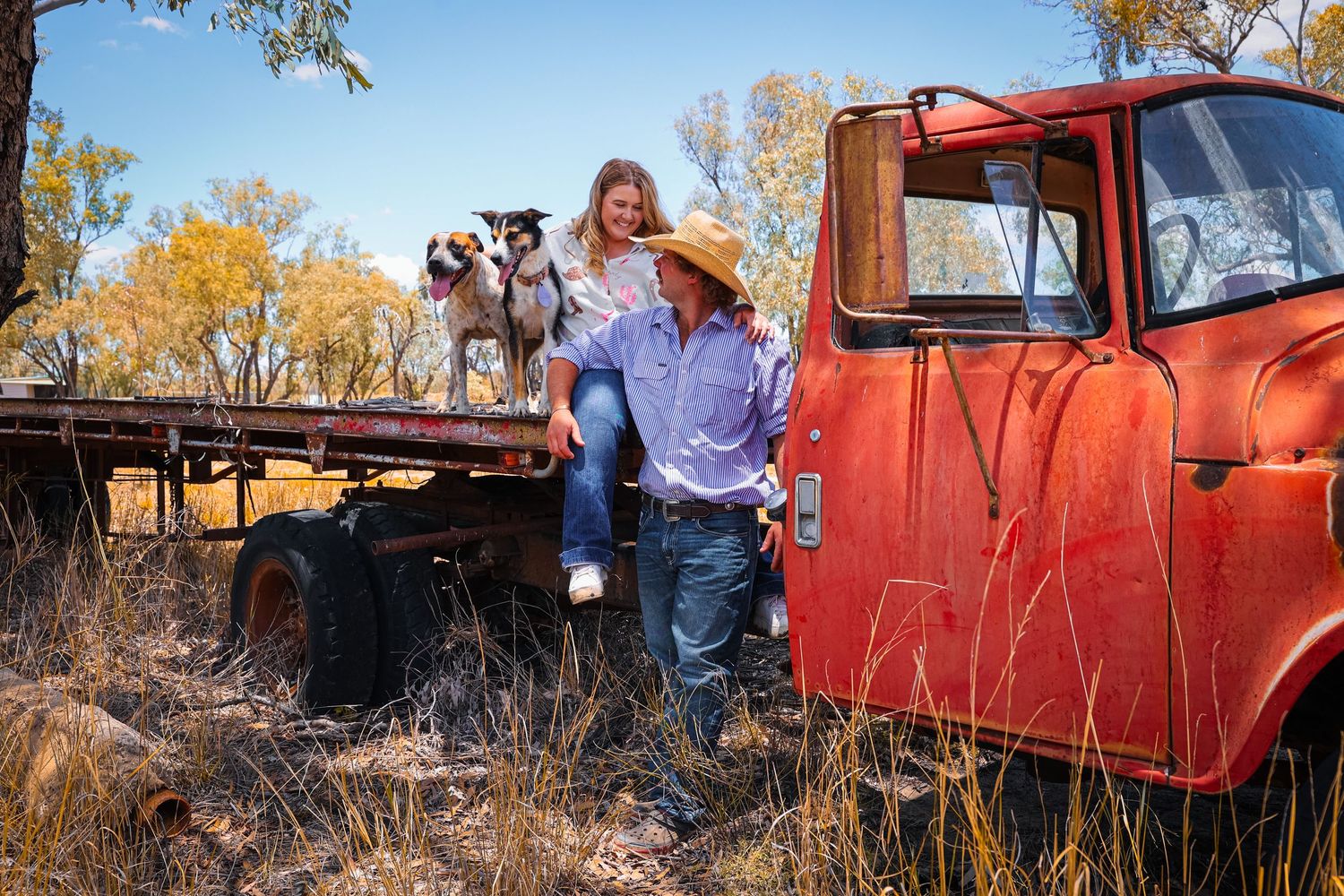 A colorful scene with people gathered around a bright red vintage truck in a rustic outdoor setting.