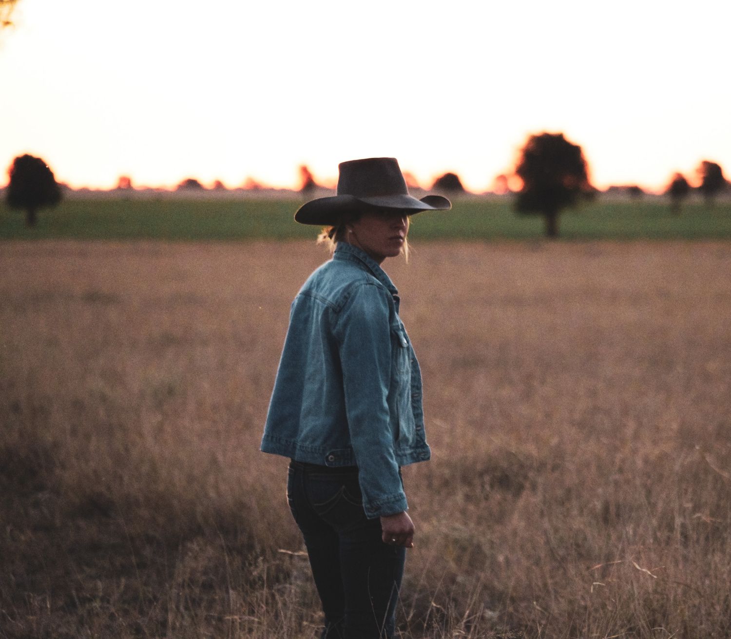 Person in western wear walking through a golden field at sunset.