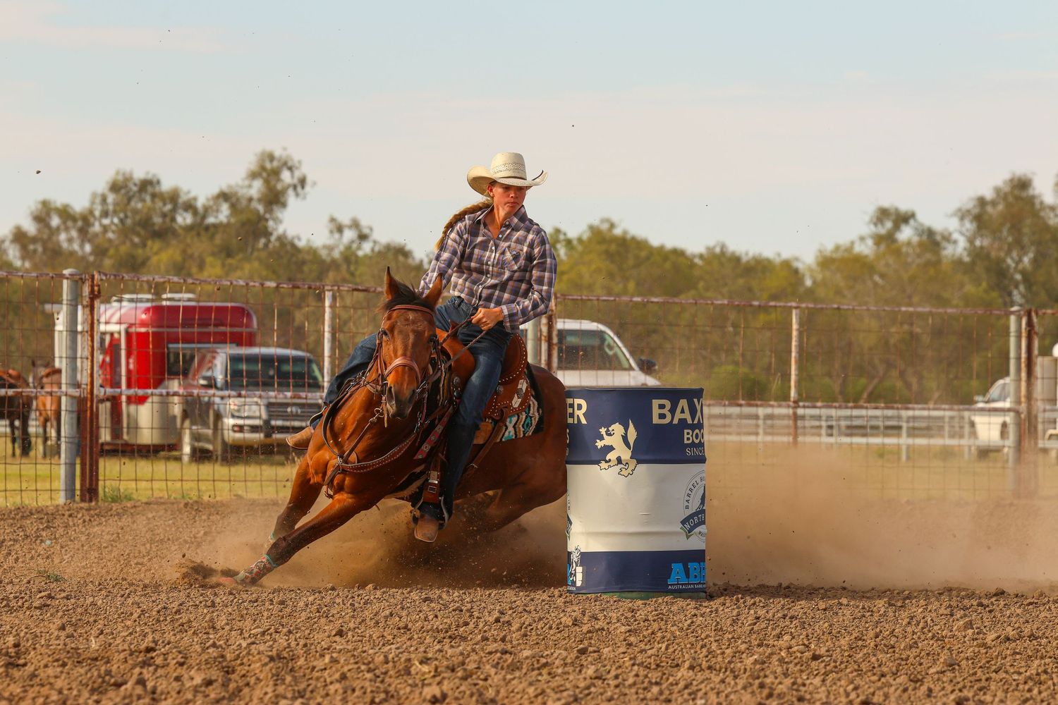 A rodeo barrel racer guides their horse around a barrel in an outdoor arena during a competition.