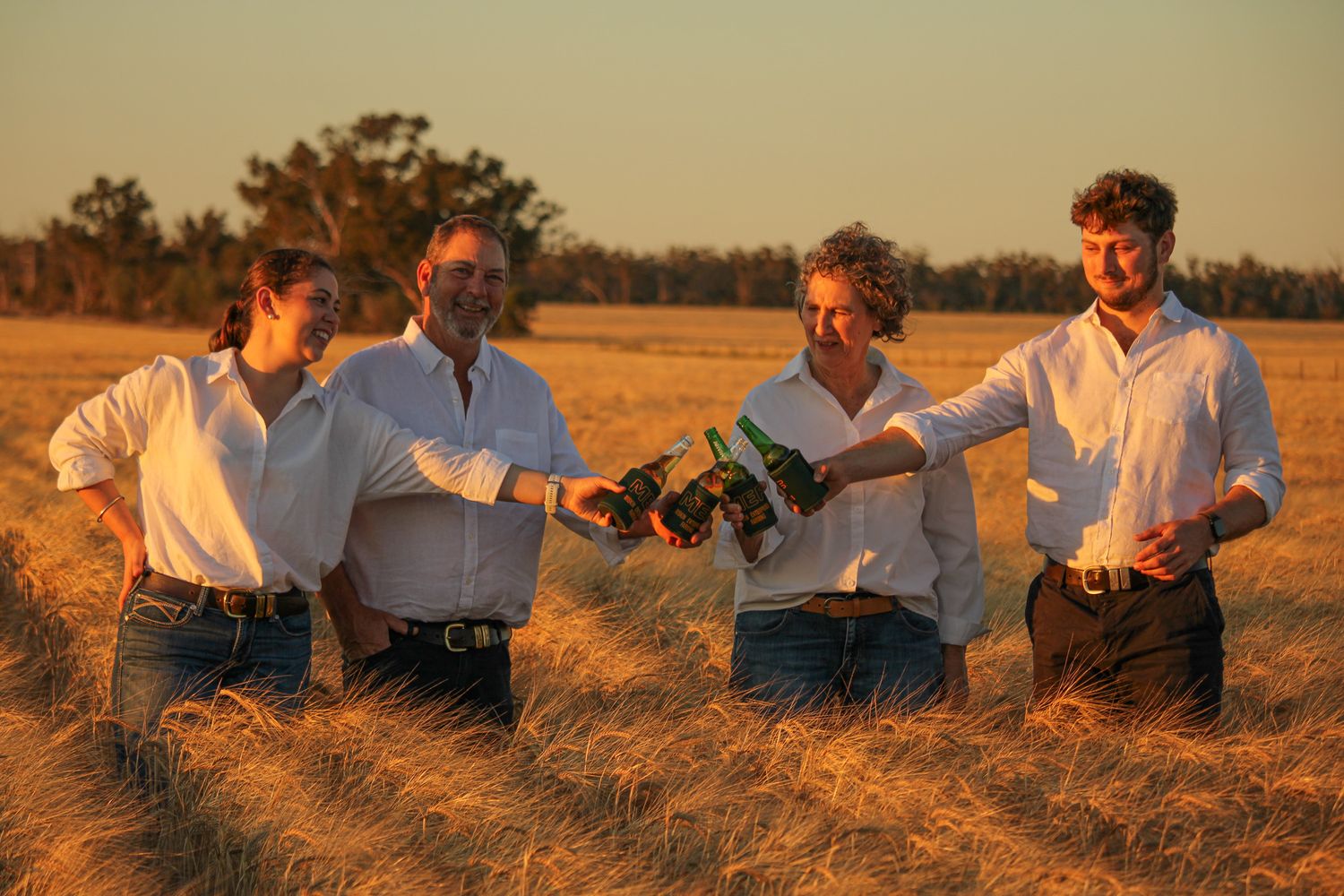 People in casual clothing sit together in a golden wheat field at sunset.