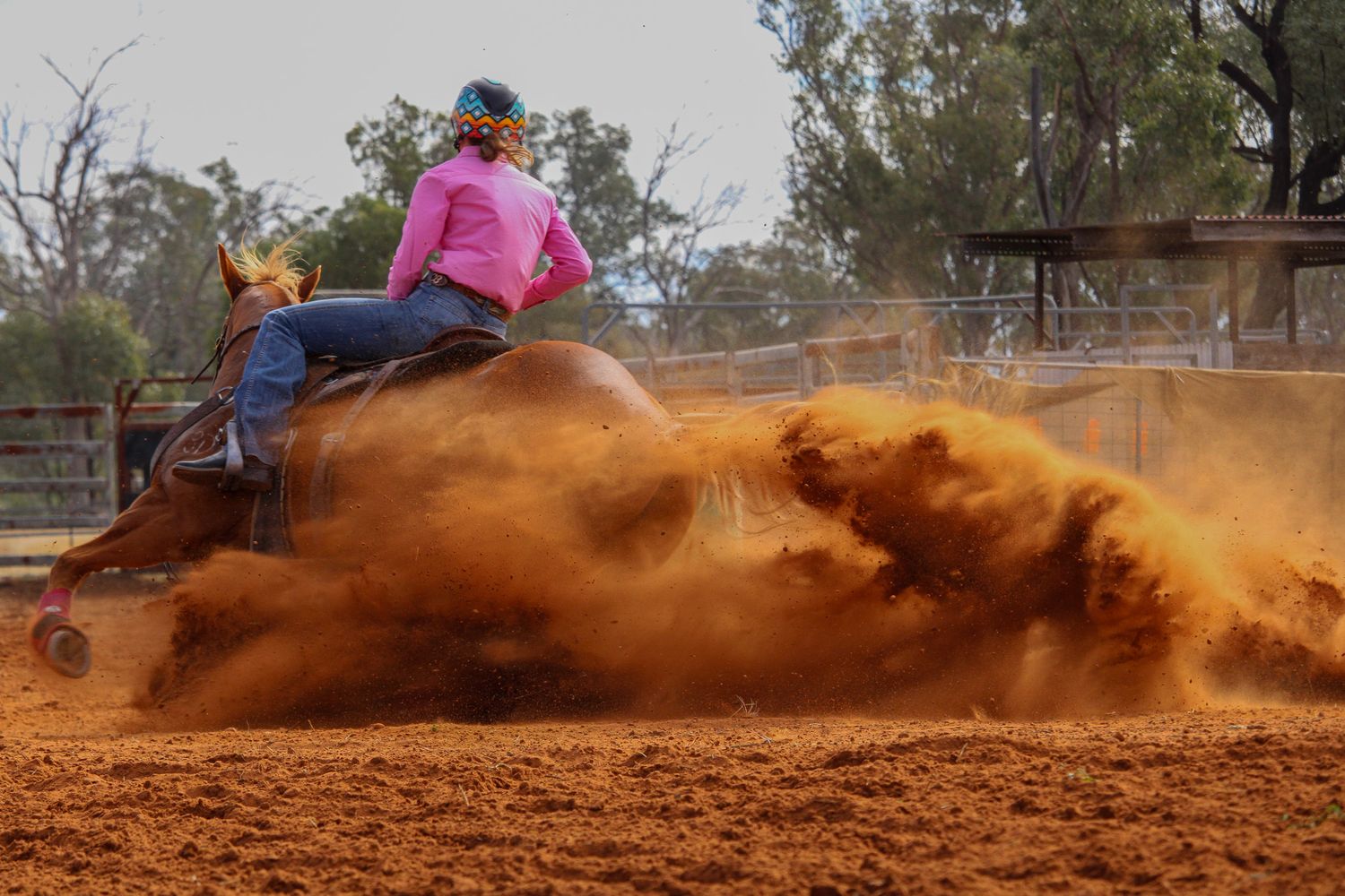 Horse racing through sandy arena creating dramatic dust clouds during competition.