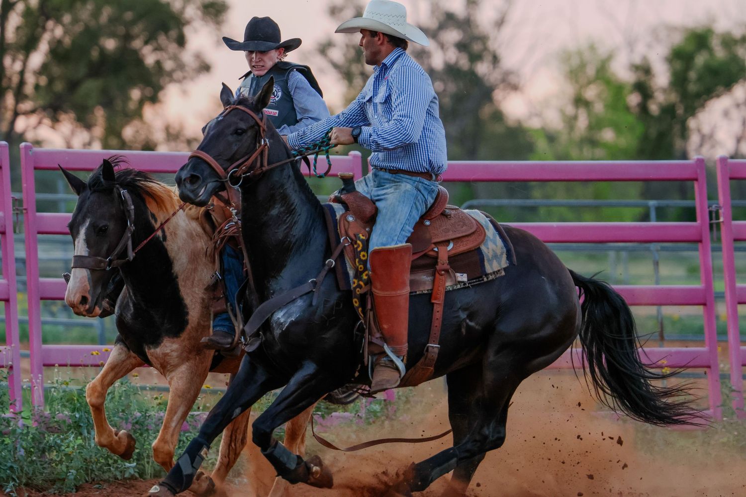 Rodeo riders on horseback compete in a fast-paced event at a western arena with pink fencing.