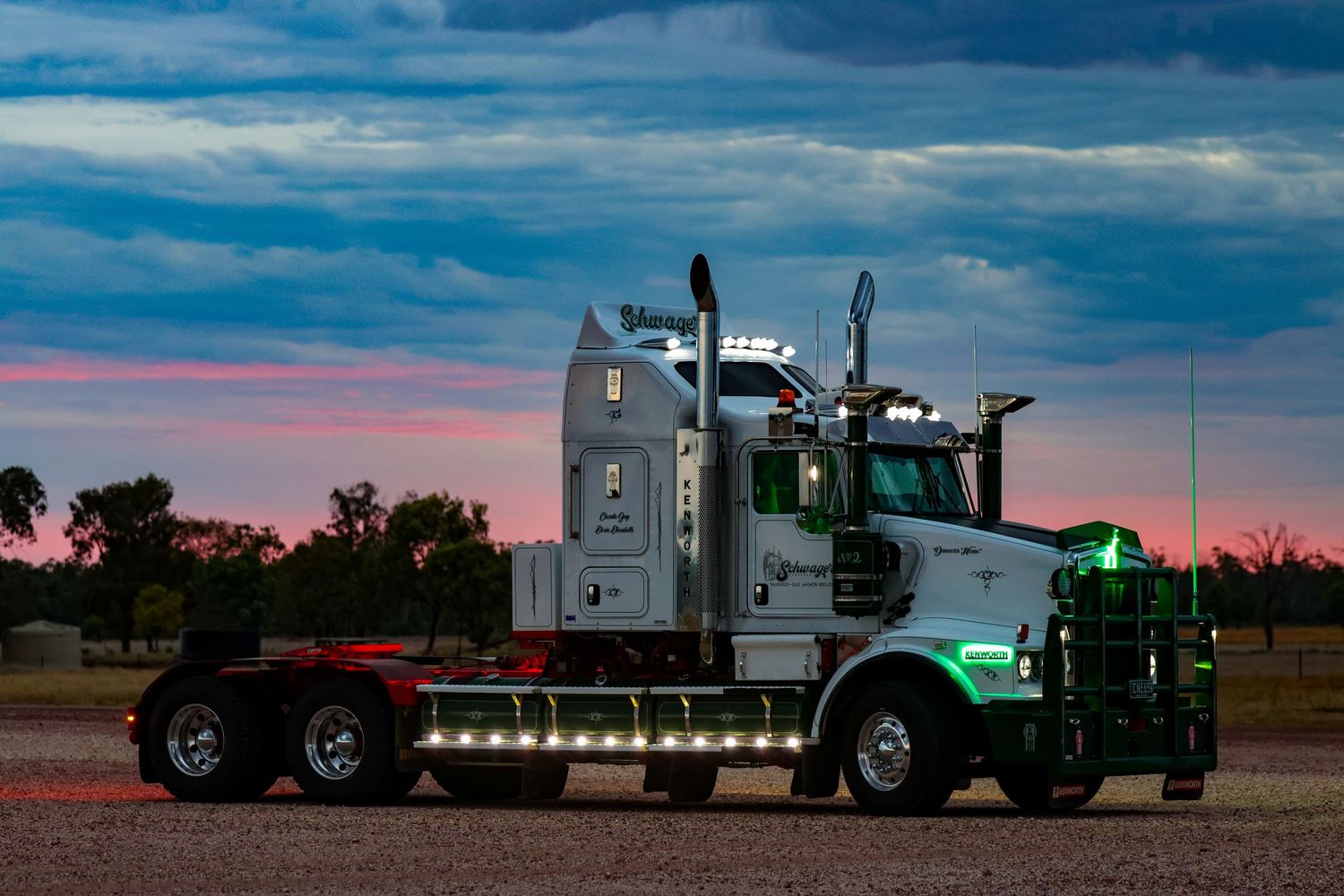 A custom Kenworth semi truck illuminated at sunset with dramatic blue and pink sky in the background.