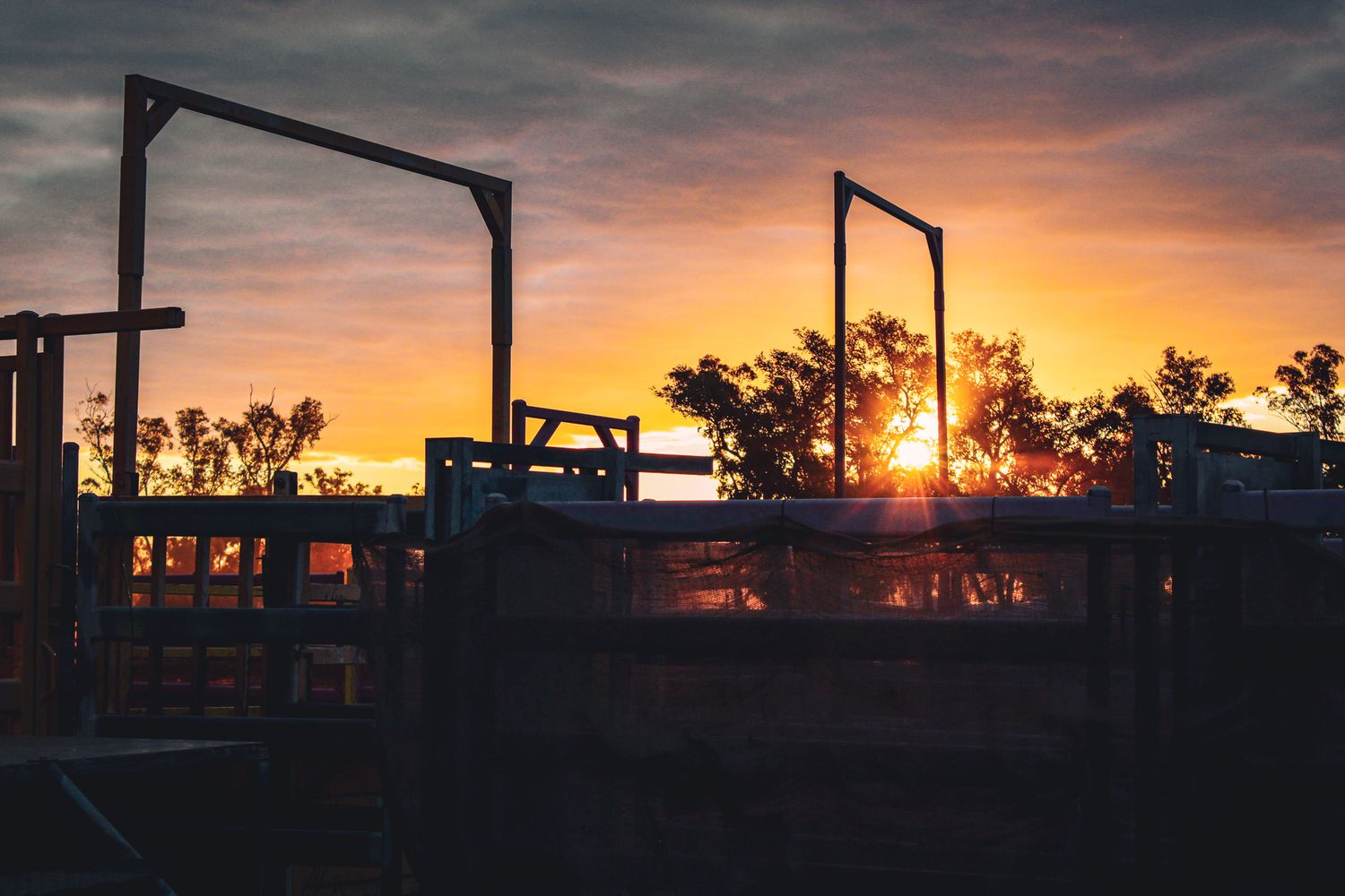 A dramatic sunset silhouettes industrial equipment and structures against an orange and purple sky.