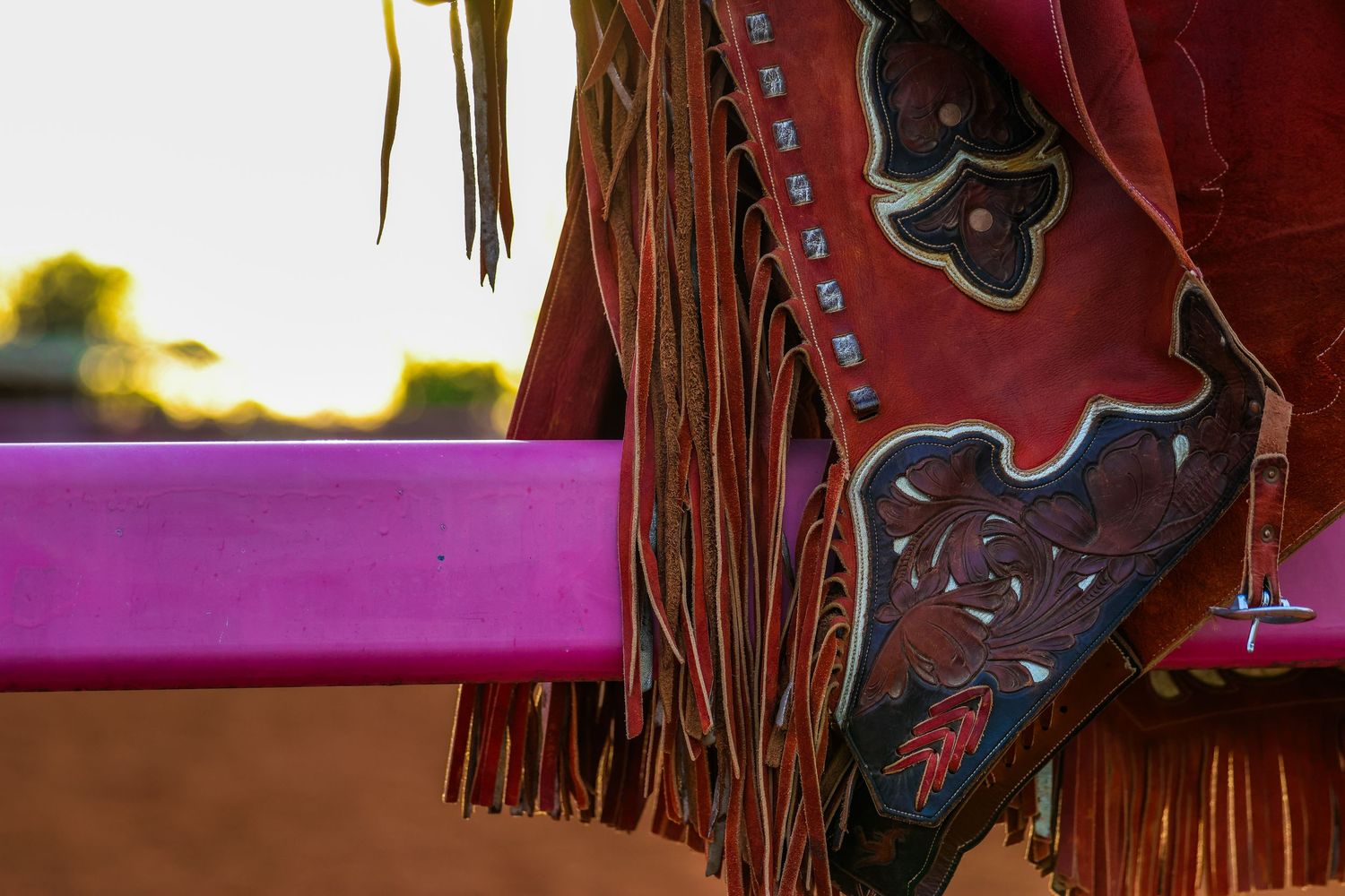 Close-up detail of brown leather cowboy boots with decorative fringe and red stitching against a dark background.