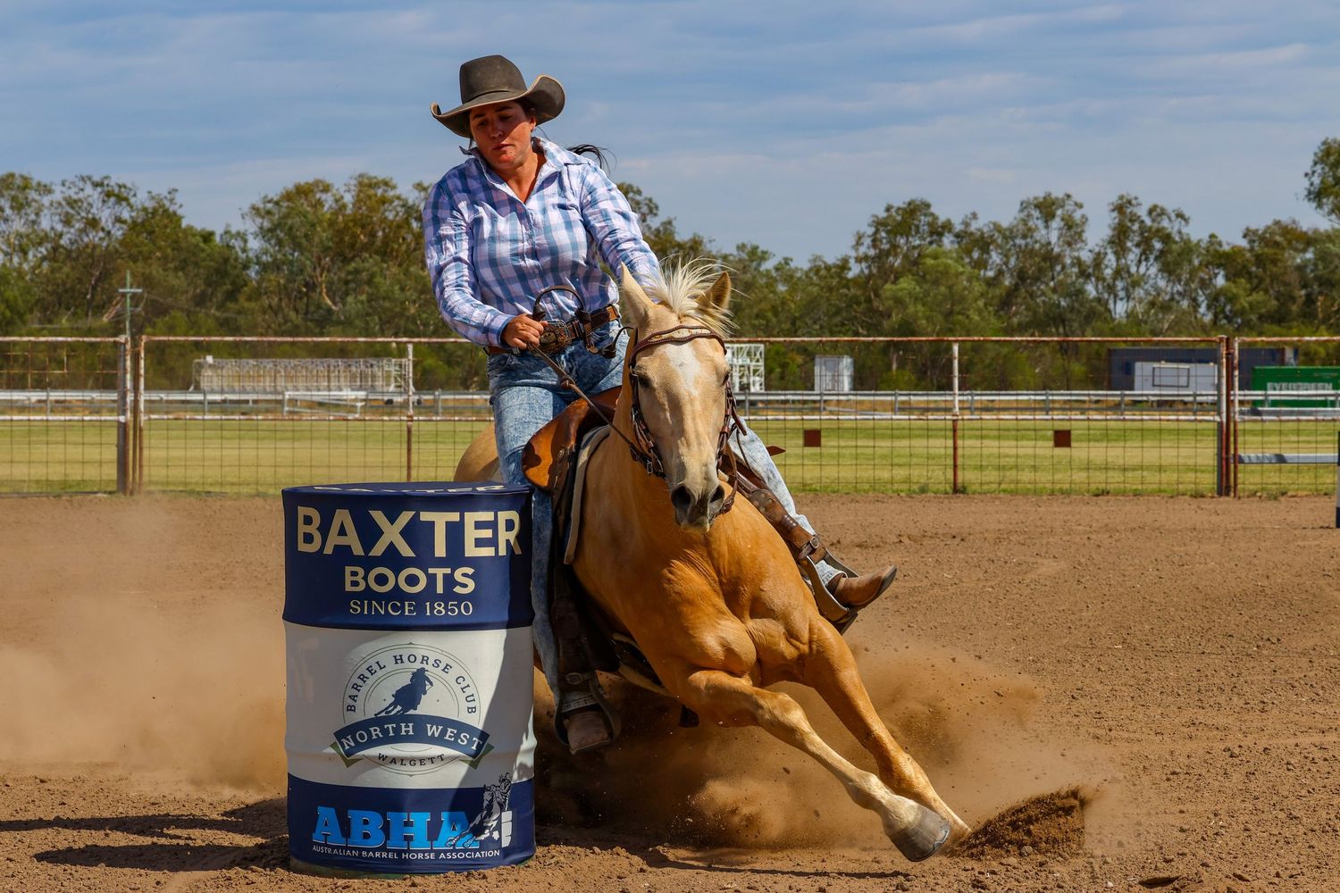 A cowboy competes in a western rodeo barrel racing event, kicking up dust in an outdoor arena.